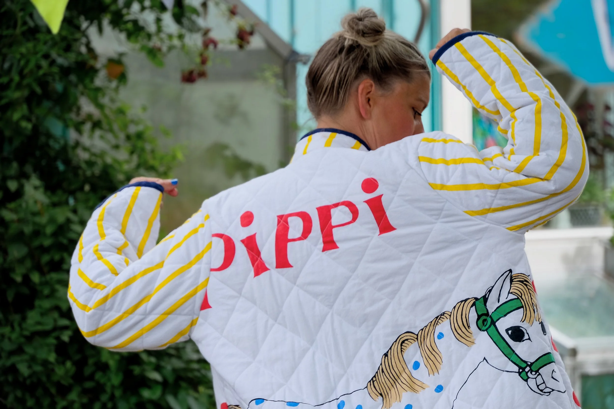 Kvinde viser sine armbue i en hvid jakke med gule striber og et foto af en pony hængende bagpå jakken