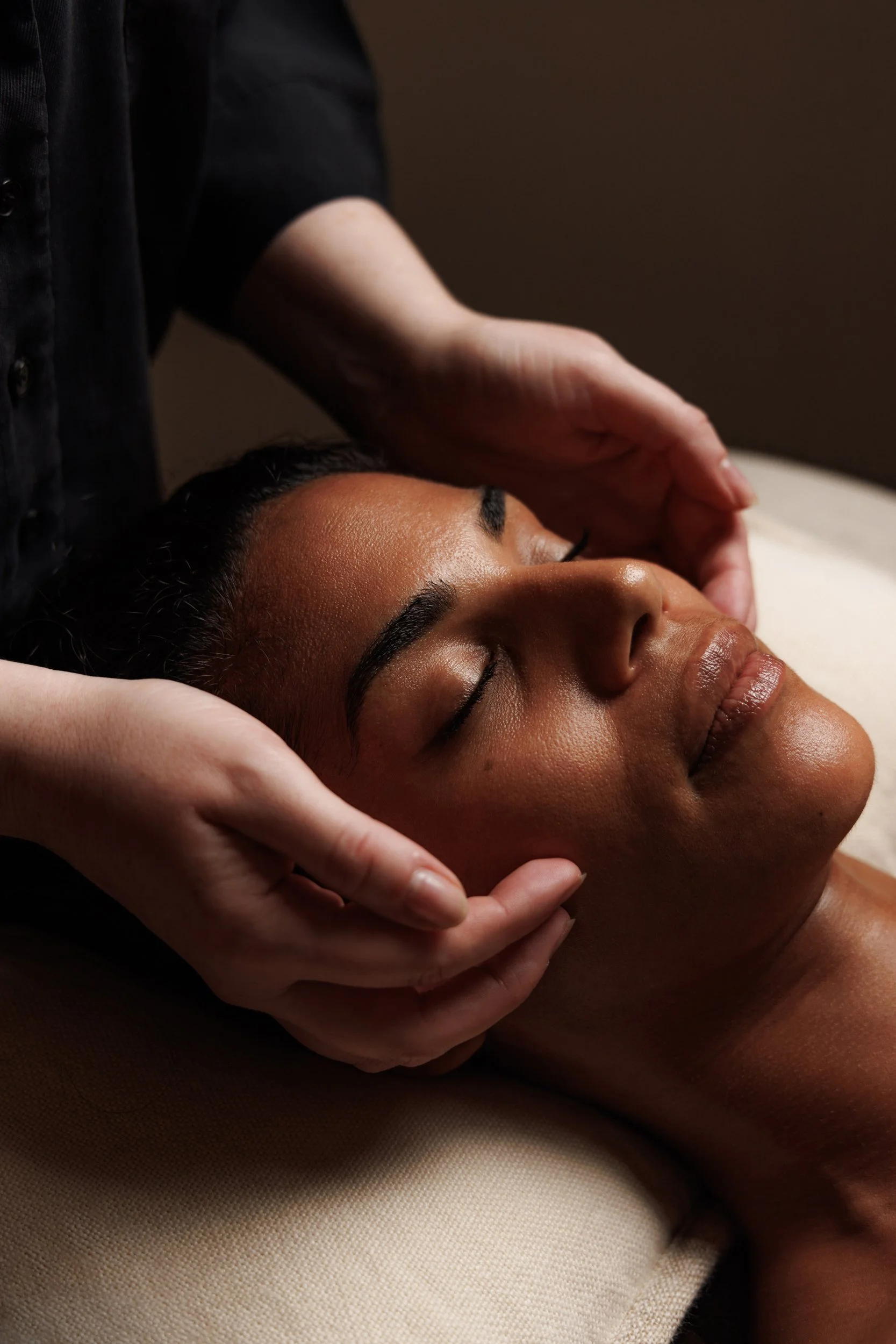 A person receiving a facial massage while lying down, with their eyes closed, someone gently pressing their forehead.