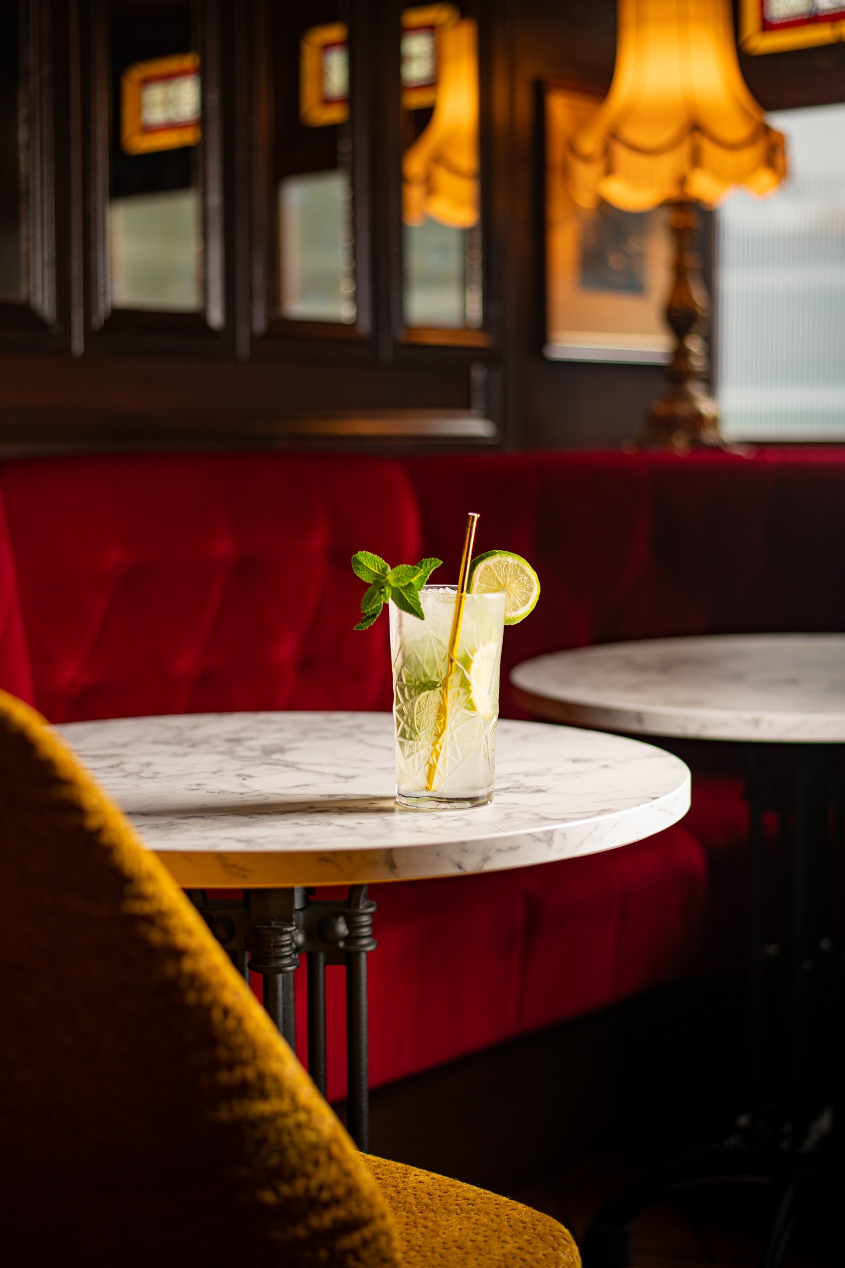 A glass of lemonade garnished with lemon slices and mint leaves on a marble table in a restaurant with red upholstered seating and dark wood paneling.