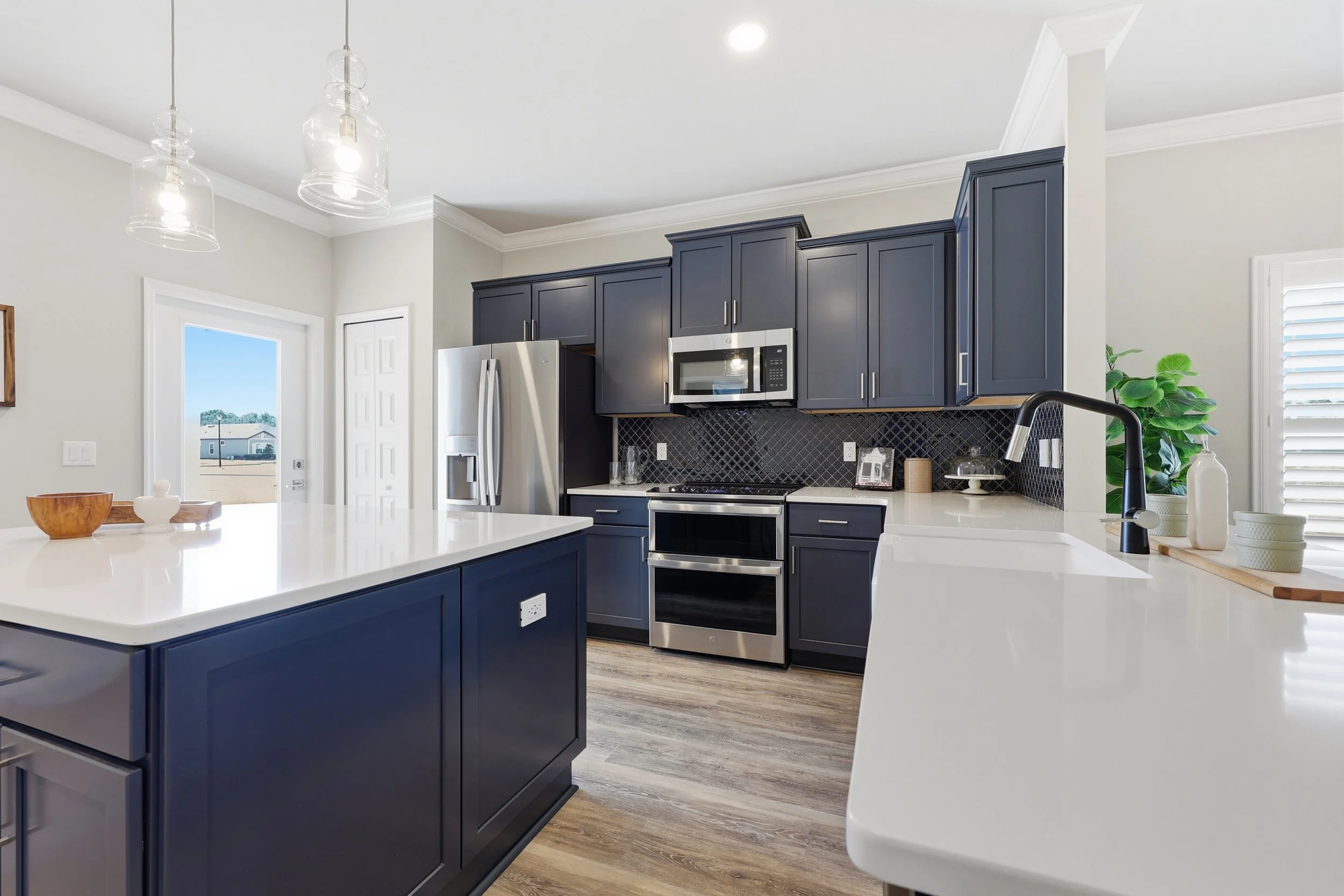 The Sicily models modern kitchen with navy blue cabinets, pendant lights, white countertops and wood floors. Bright and airy with natural light, this is the perfect kitchen for entertaining.