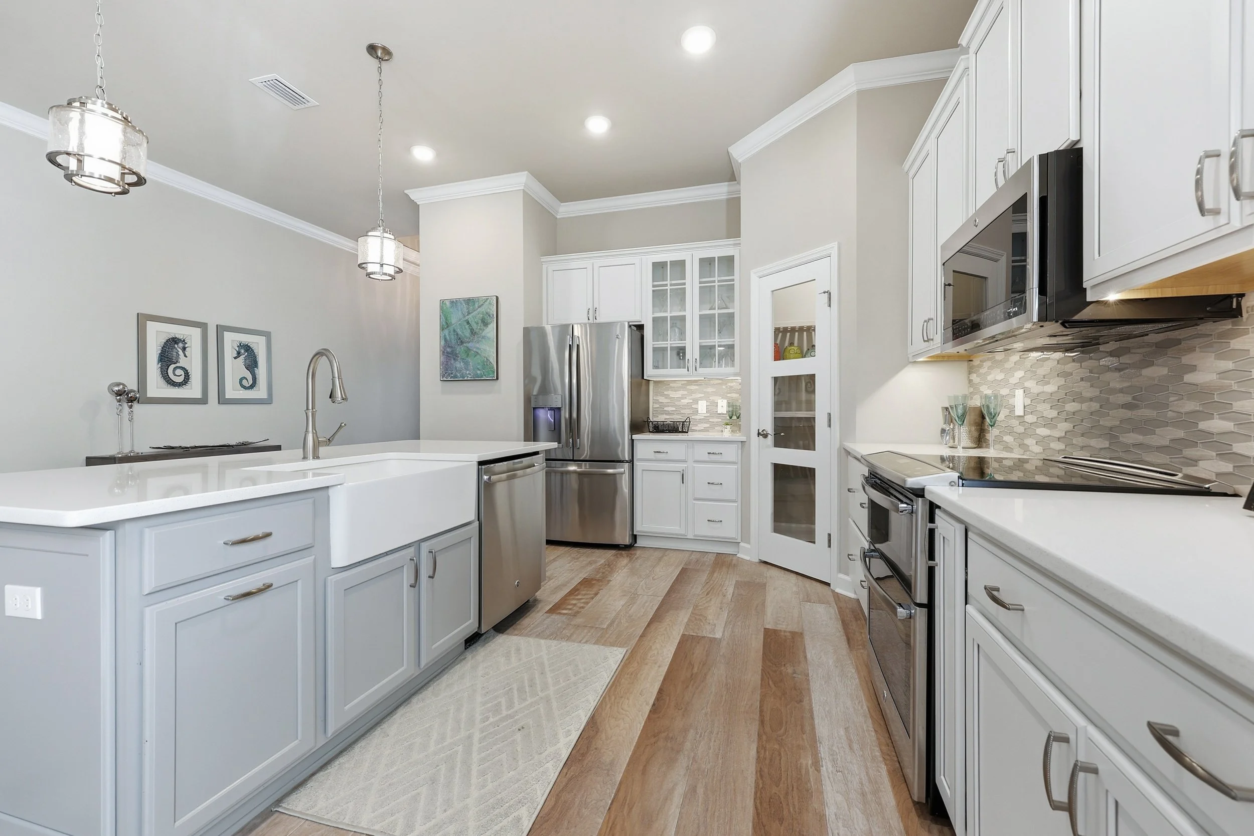 Bright modern kitchen with island, white cabinets, pendant lights, and stainless steel appliances.