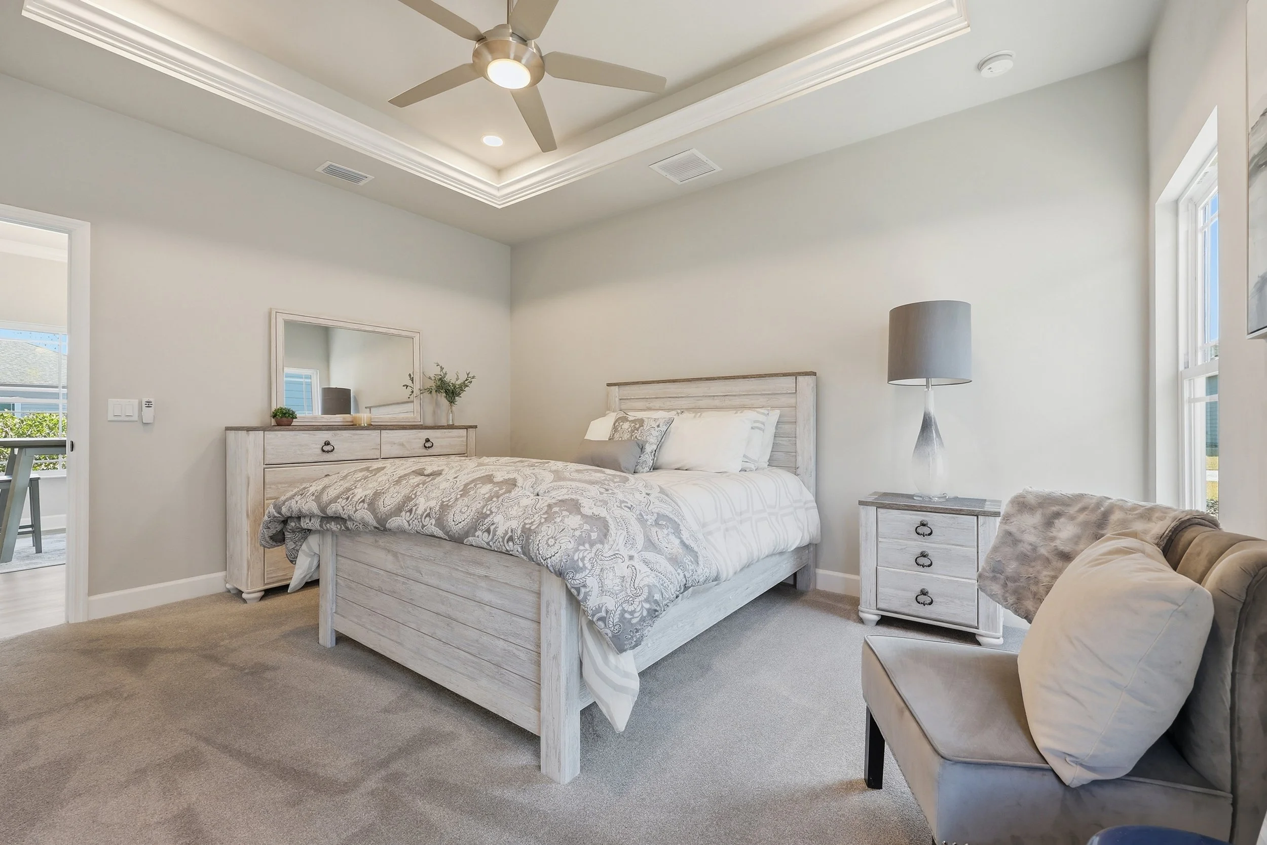 Primary bedroom in the Messina model with lots of natural light, tray ceiling, ceiling fan and luxury carpet.