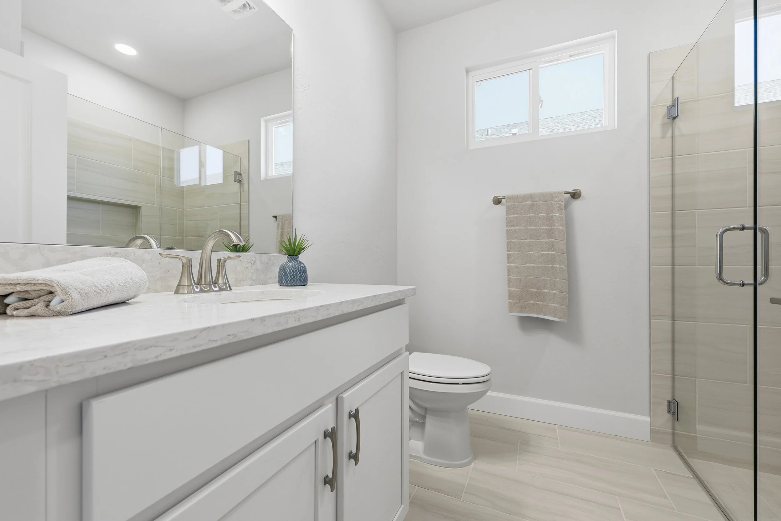 Guest bathroom in Lucca model with white vanity, large walk-in shower, and bright natural light coming from transom window