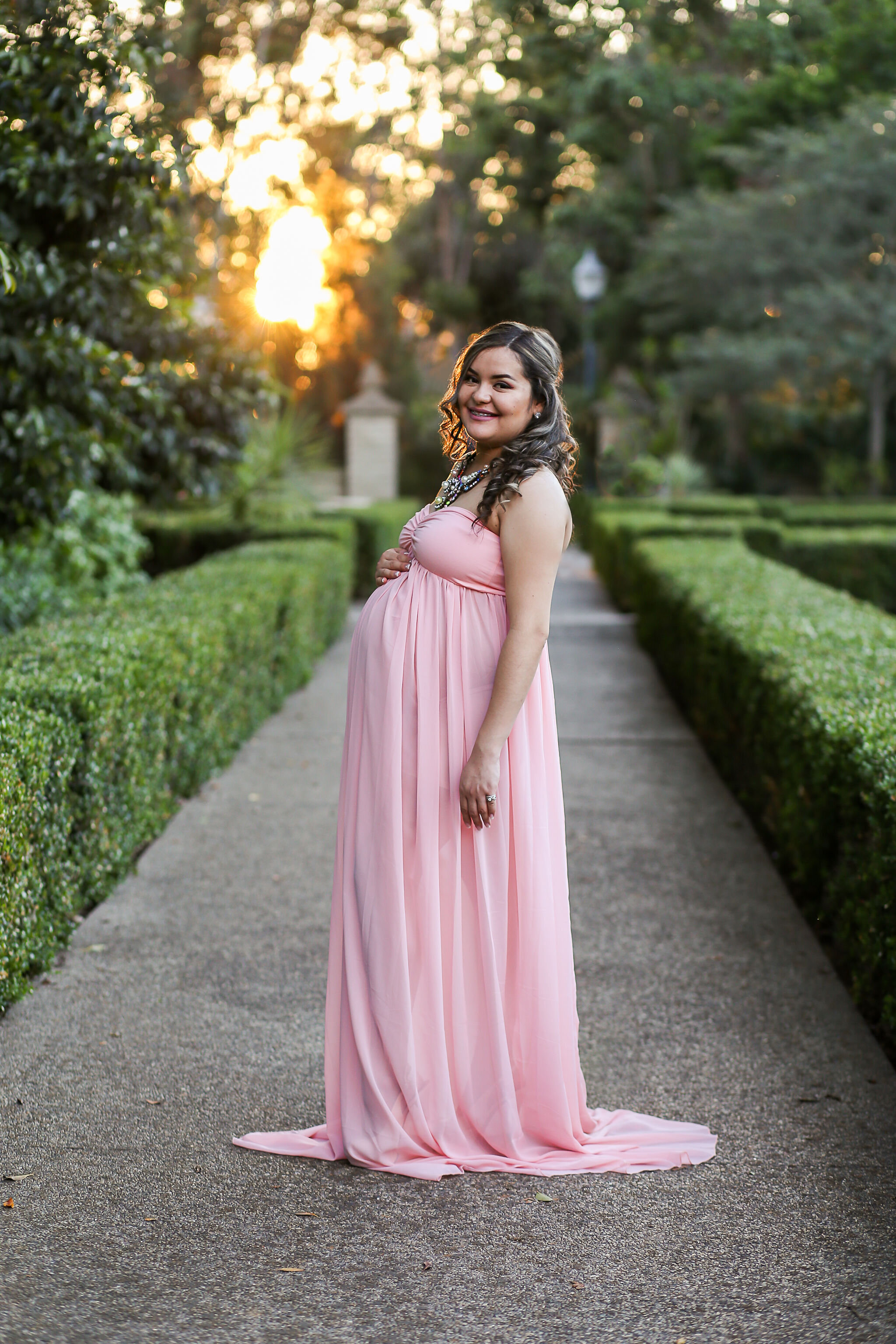 a beautiful mother-to-be stands in a park in a pink dress by Laura Rose, a maternity photographer in San Diego, CA