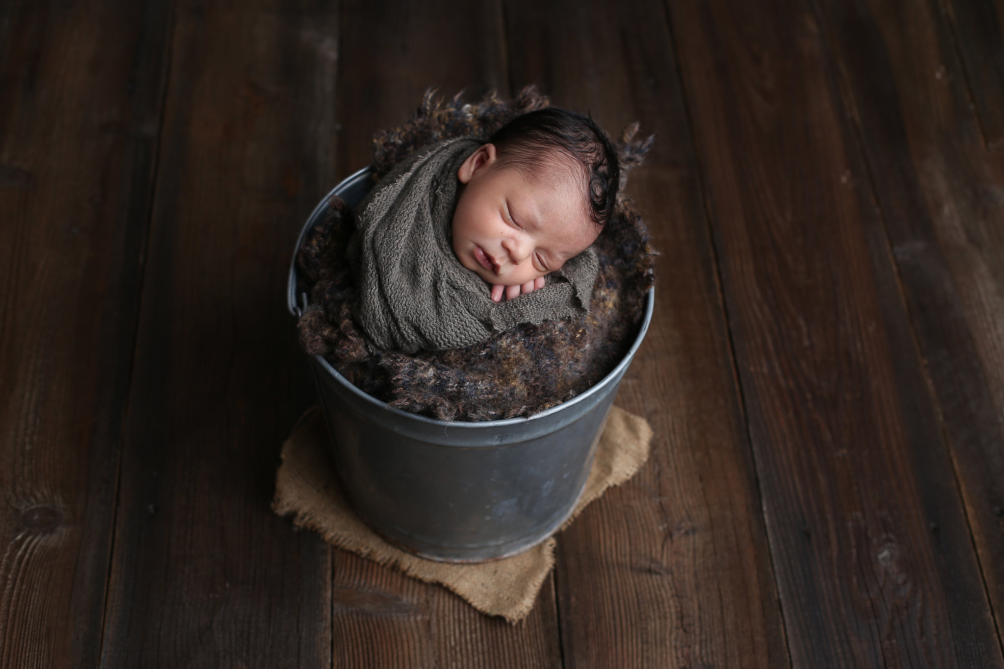 a newborn baby sleeps peacefully in a vintage metal bucket in this newborn photography session