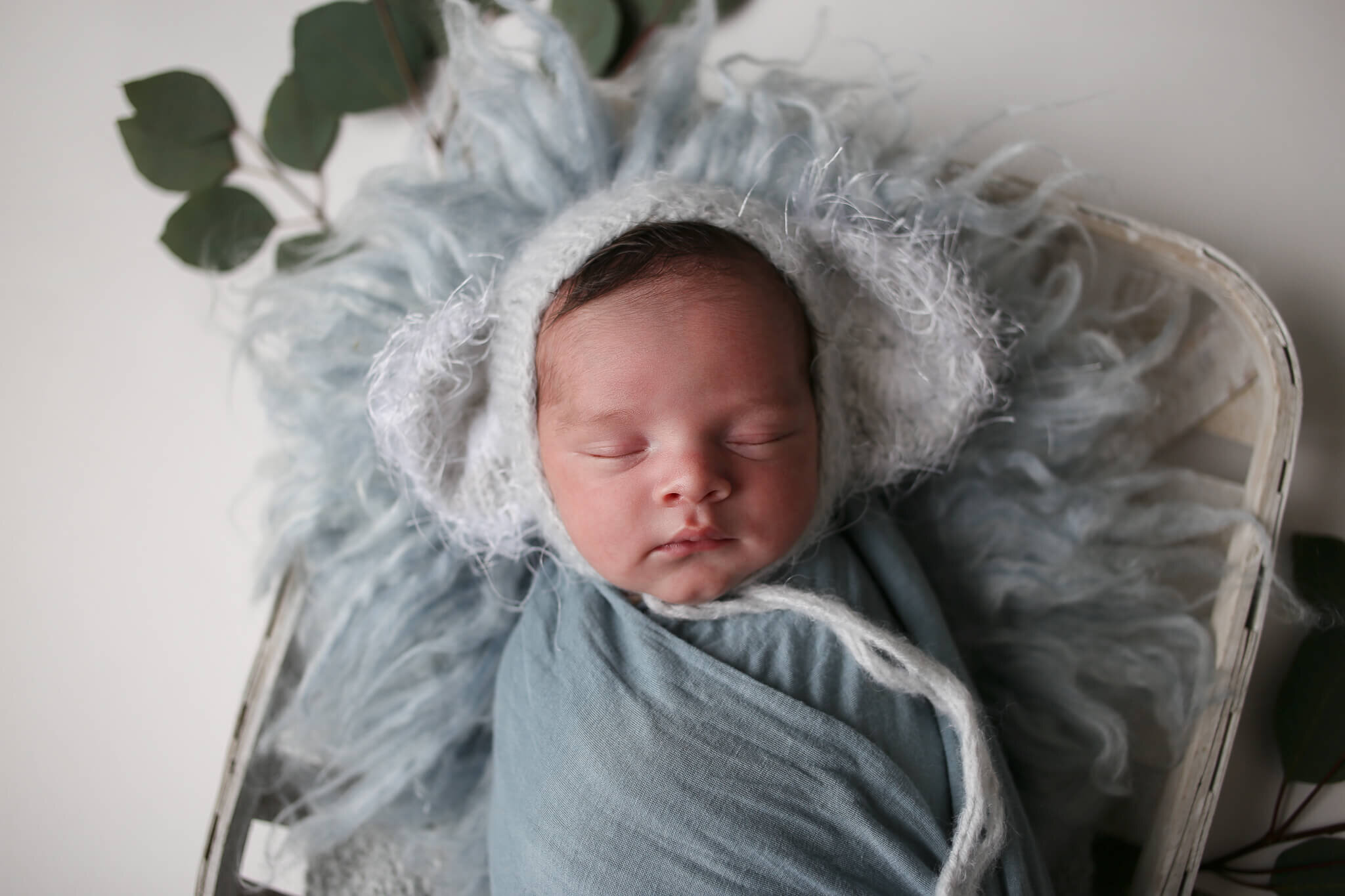  An image of a tiny newborn wrapped in gauze and sweetly sleeping in a knitted cap with big fuzzy mouse ears while his head rests on a soft cushion of yarn by Photography by L Rose - San Diego newborn photography 