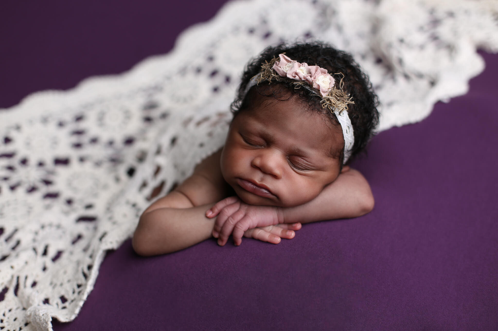  A picture of a newborn girl in her flowered headband, sleeping on her tummy with her cheek resting on her arms, covered in a crocheted blanket by Photography by L Rose - San Diego CA newborn photography 