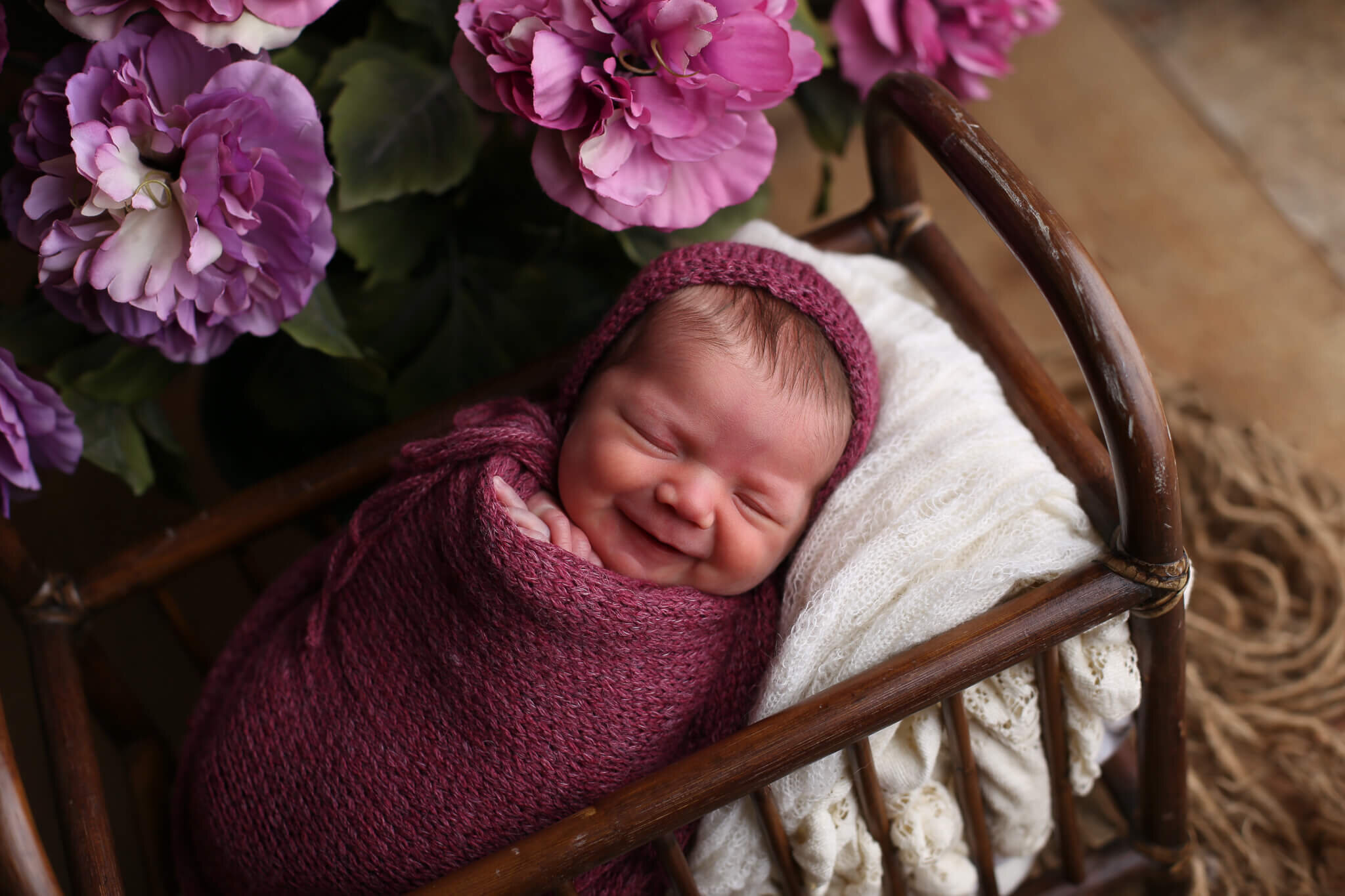  A picture of a smiling newborn baby, wrapped tight in a blanket that rests in a wooden cradle as it sleeps from a baby photo session 