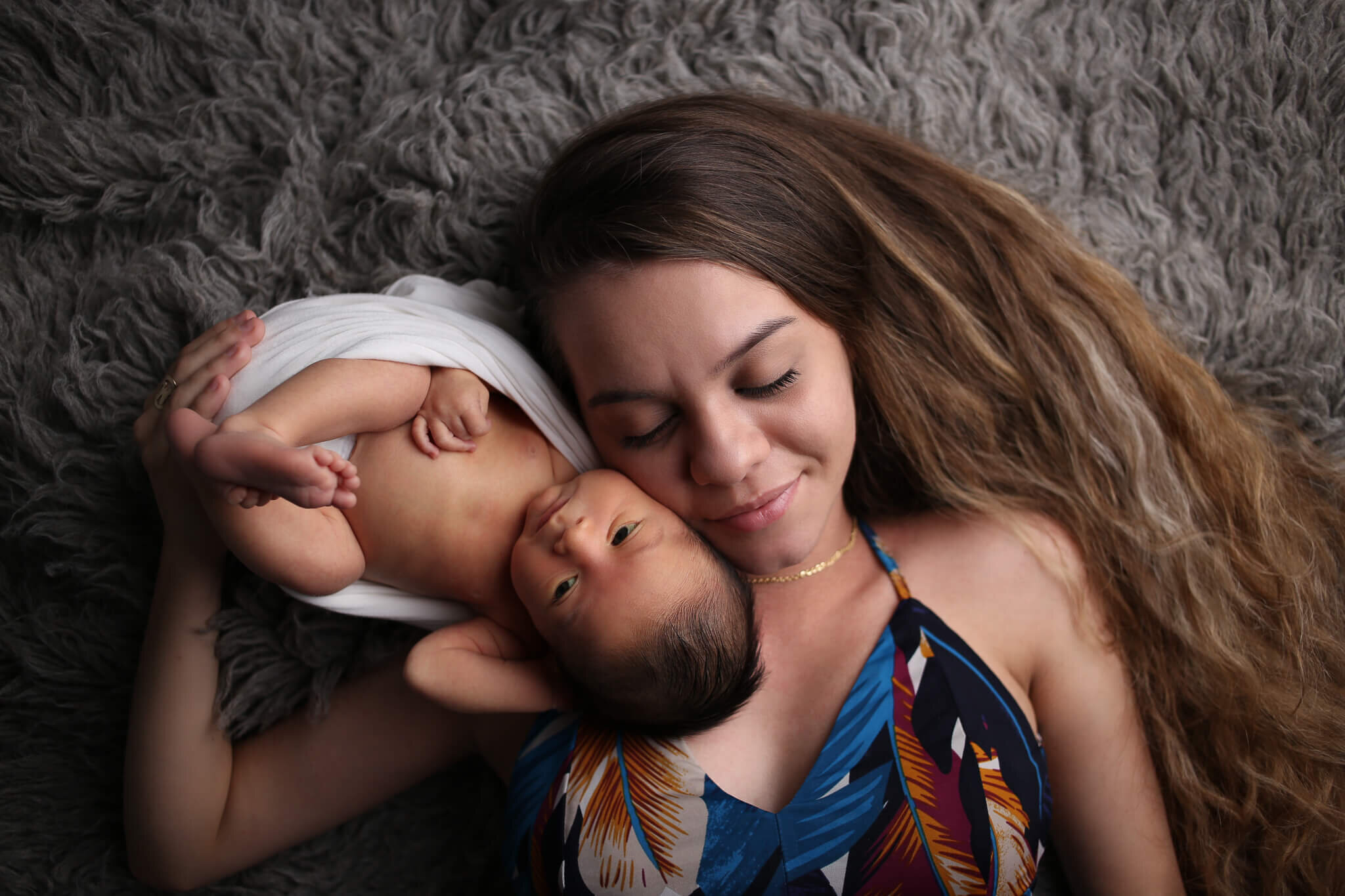  A picture of a new mother lying with her eyes closed, next to her newborn as the baby lies in the opposite direction with its head touching her cheek in a peaceful moment by Photography by L Rose in San Diego 