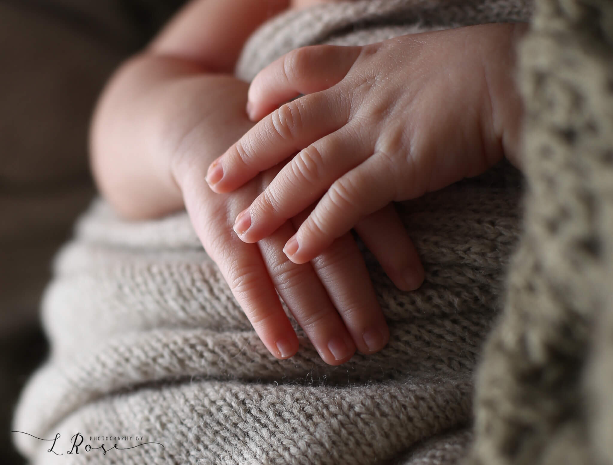  An image of a closeup view of a newborn baby’s tiny hands resting on a knitted blanket, lit up by glowing light from a newborn picture session 