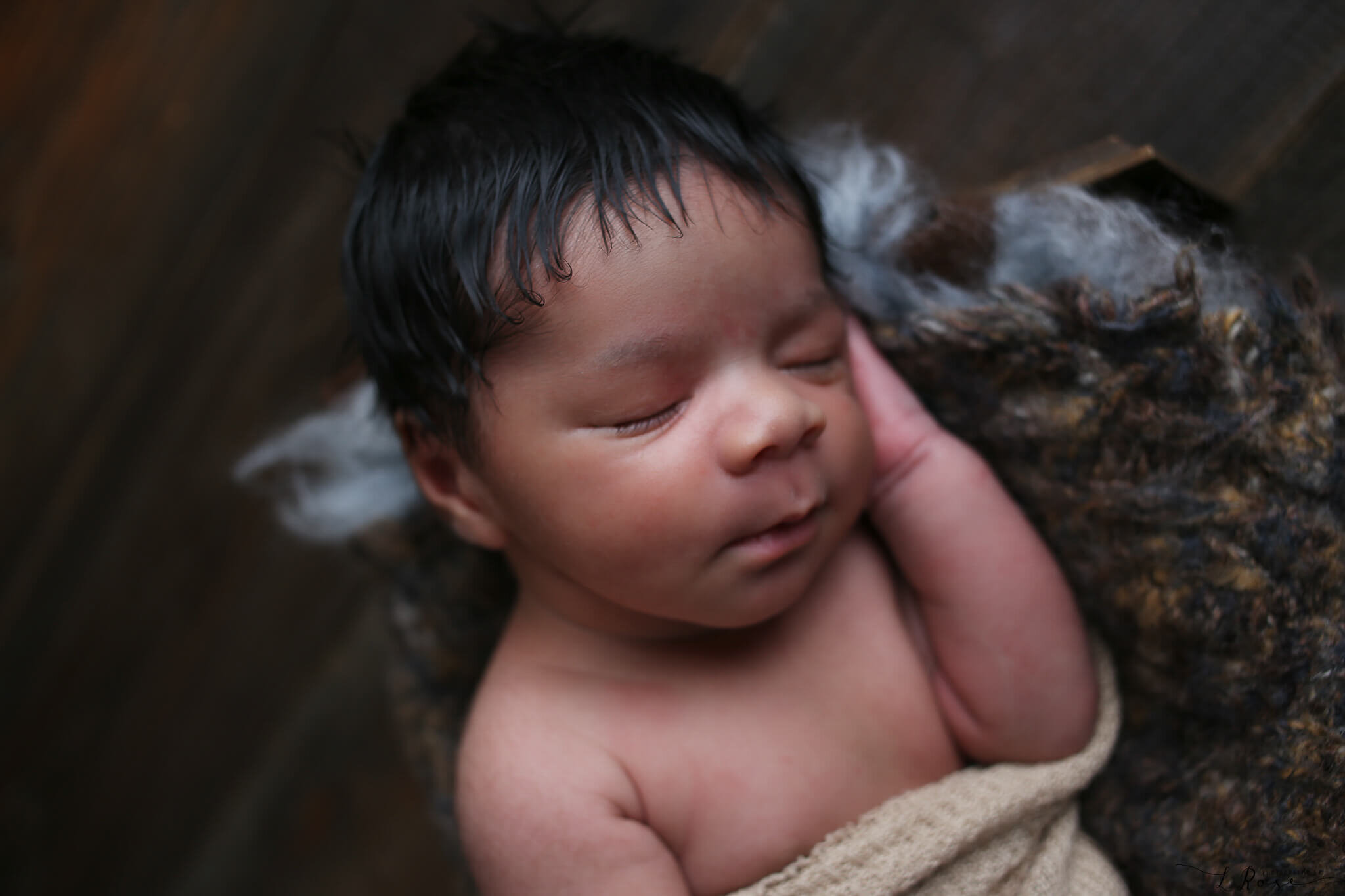  An image of a newborn baby up close, sleeping peacefully with one hand up next to its cheek, resting in soft blankets by Photography by L Rose 