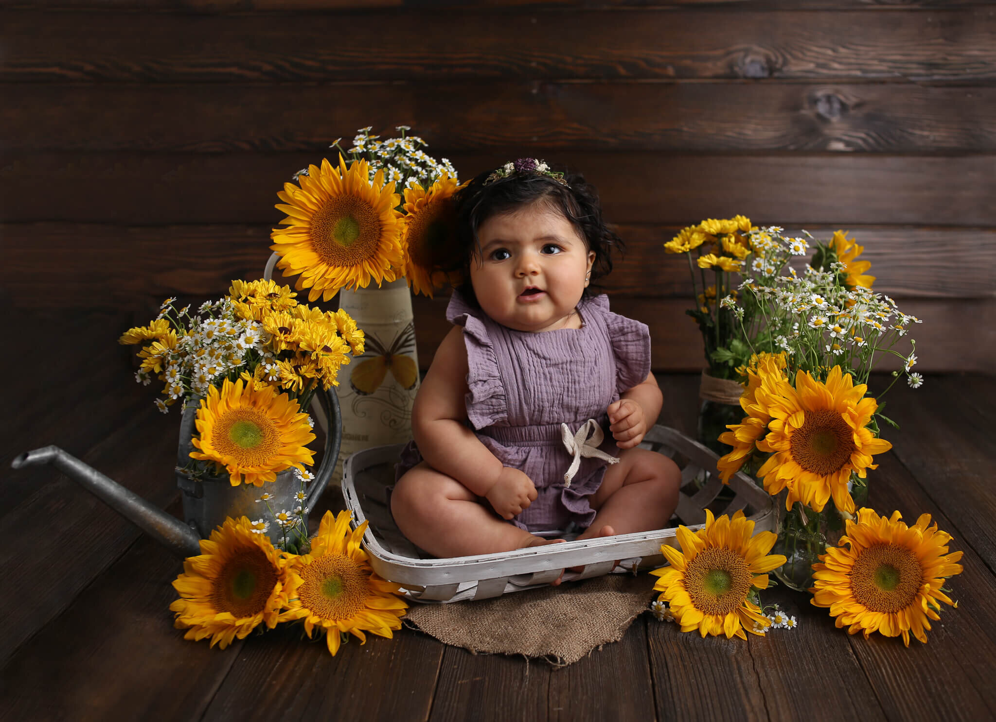  An image of a baby girl dressed in a ruffled short playsuit, sitting in a basket surrounded by cheerful sunflowers and daisies, marking an important milestone by Photography by L Rose, baby photography in San Diego 