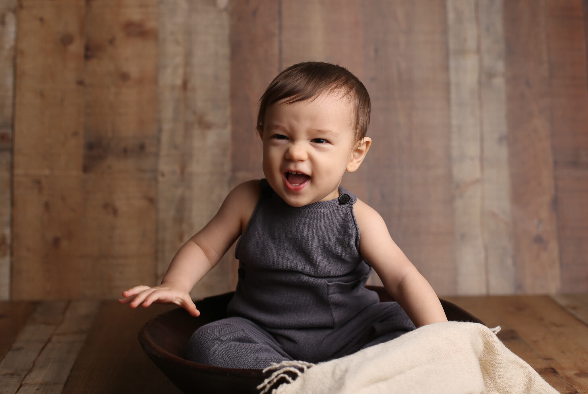  A picture of a baby boy with a cute sneer that wrinkles his nose as he sits in a bowl in a cute jumpsuit, reaching a milestone in his growth by Photography by L Rose, baby photography in San Diego CA 