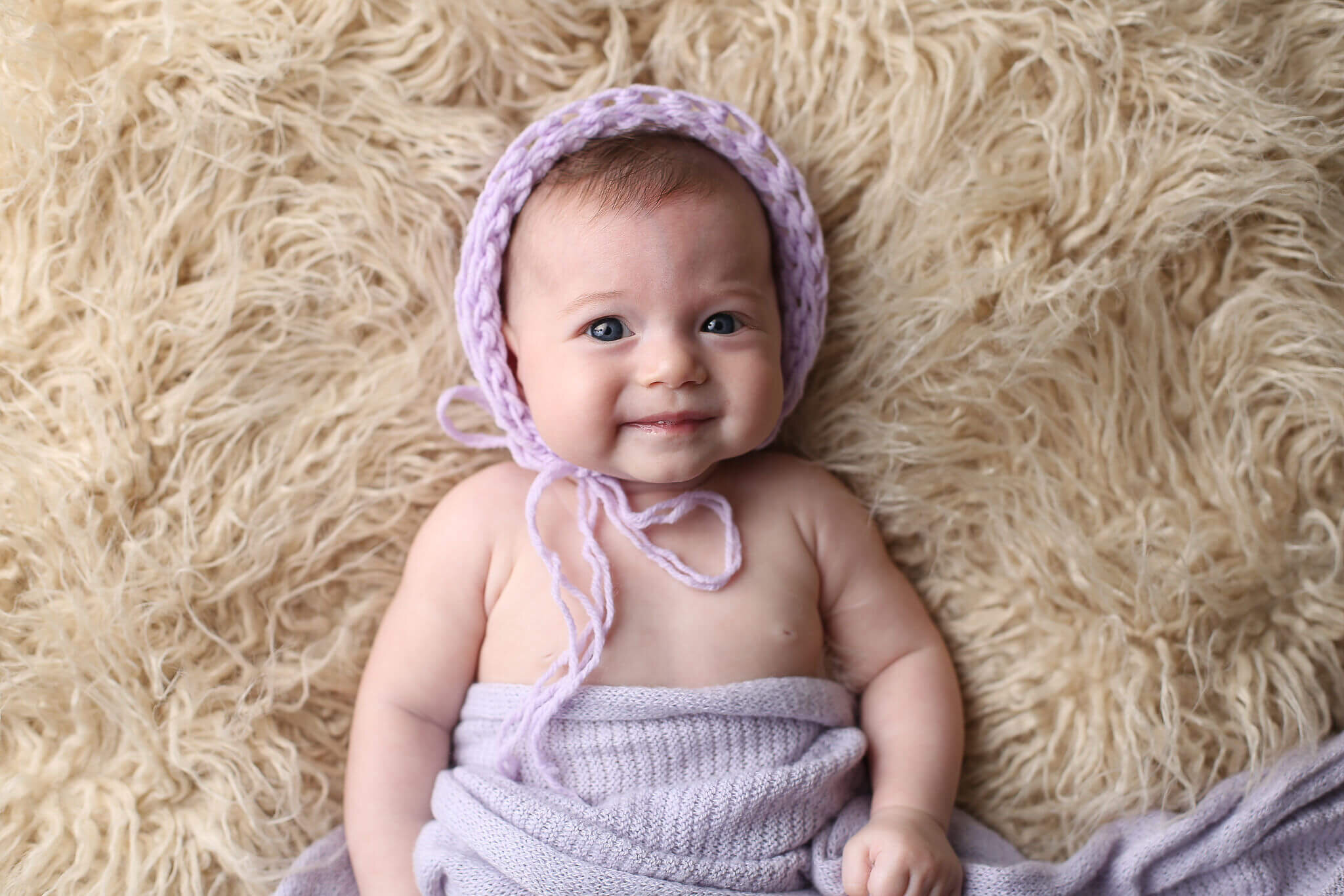  An image of a sweet baby girl in a knitted cap and blanket, gazing up at the camera with a small smile on her dainty face as she celebrates a milestone by Photography by L Rose, baby photography in San Diego 