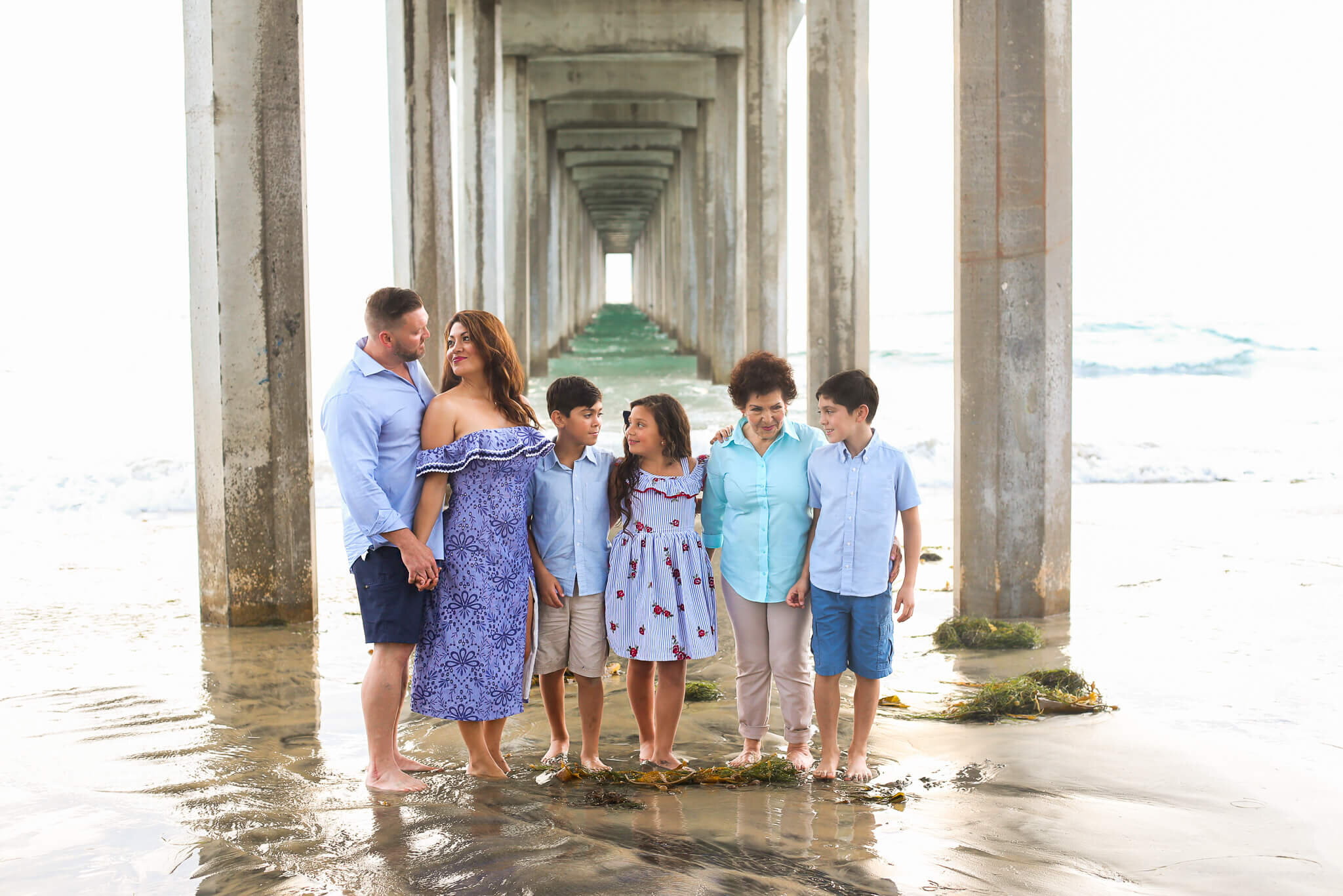  A photograph of a family standing beneath a colonnade of pillars under a pier, with the father and mother gazing fondly at each other while the three children and grandma smile together alongside them by Photography by L Rose - San Diego California 