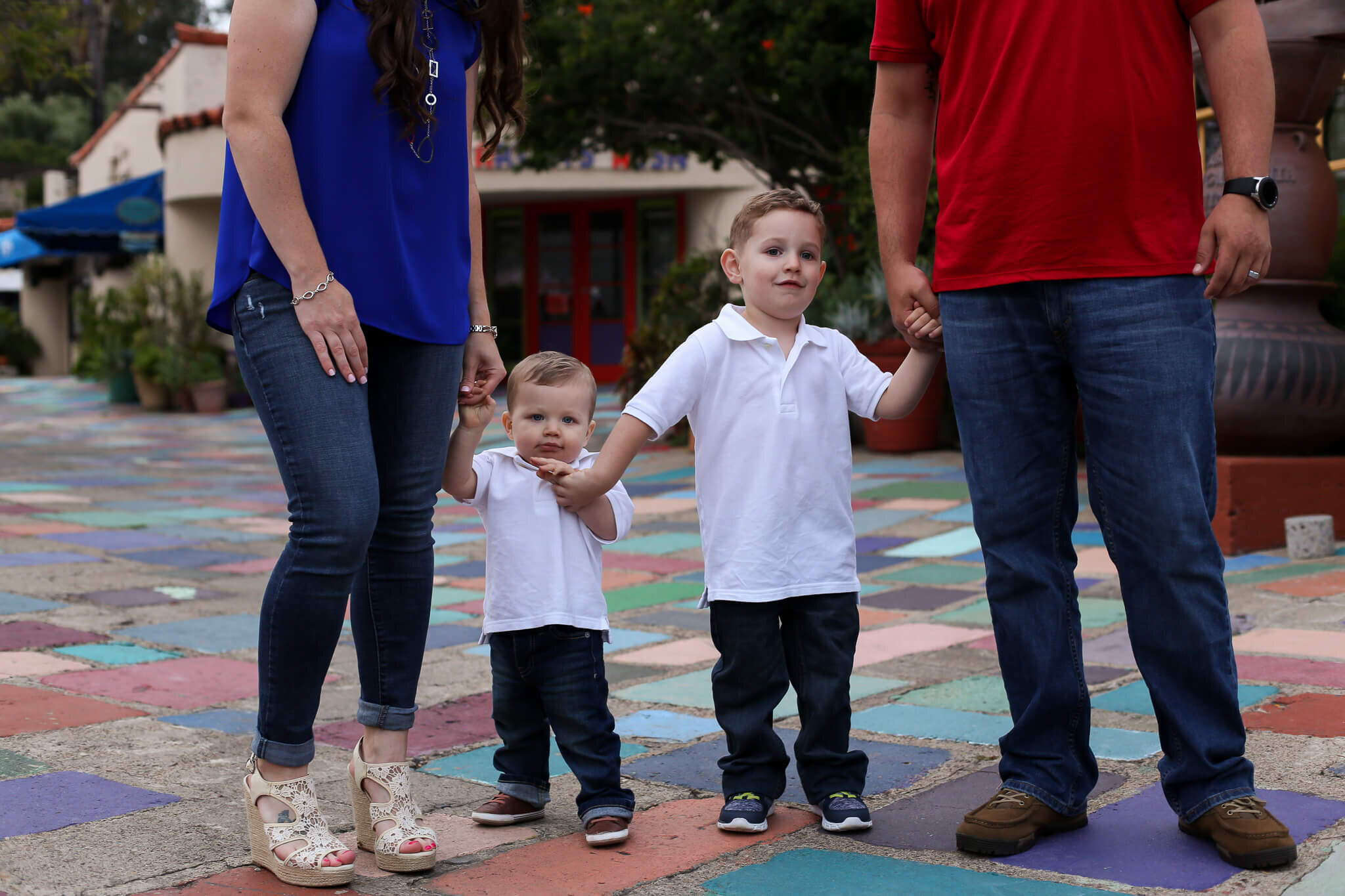  A photograph of a closeup view of mom and dad holding hands with their two young children between them, spending time together as a family at an outdoor patio by Photography by L Rose 