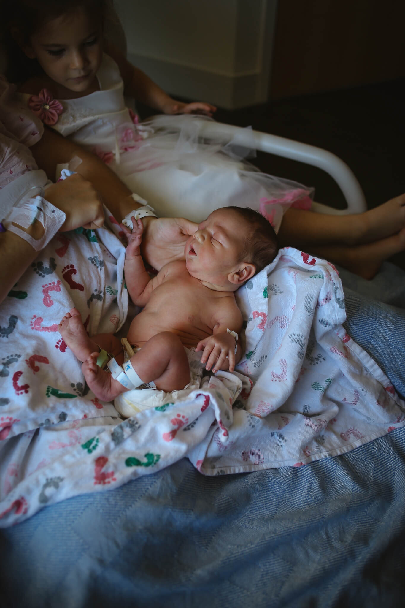  An image of a newborn baby lying in an opened blanket on mom’s lap in the recovery bed, showing his tiny belly and arms and legs with the cord clamp visible by Photography by L Rose - San Diego newborn photography 