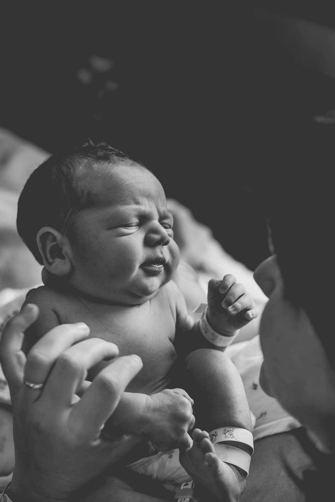  A photograph of a closeup view of a newborn baby’s expressive face with closed eyes as mom holds him up close to her from a newborn picture session 