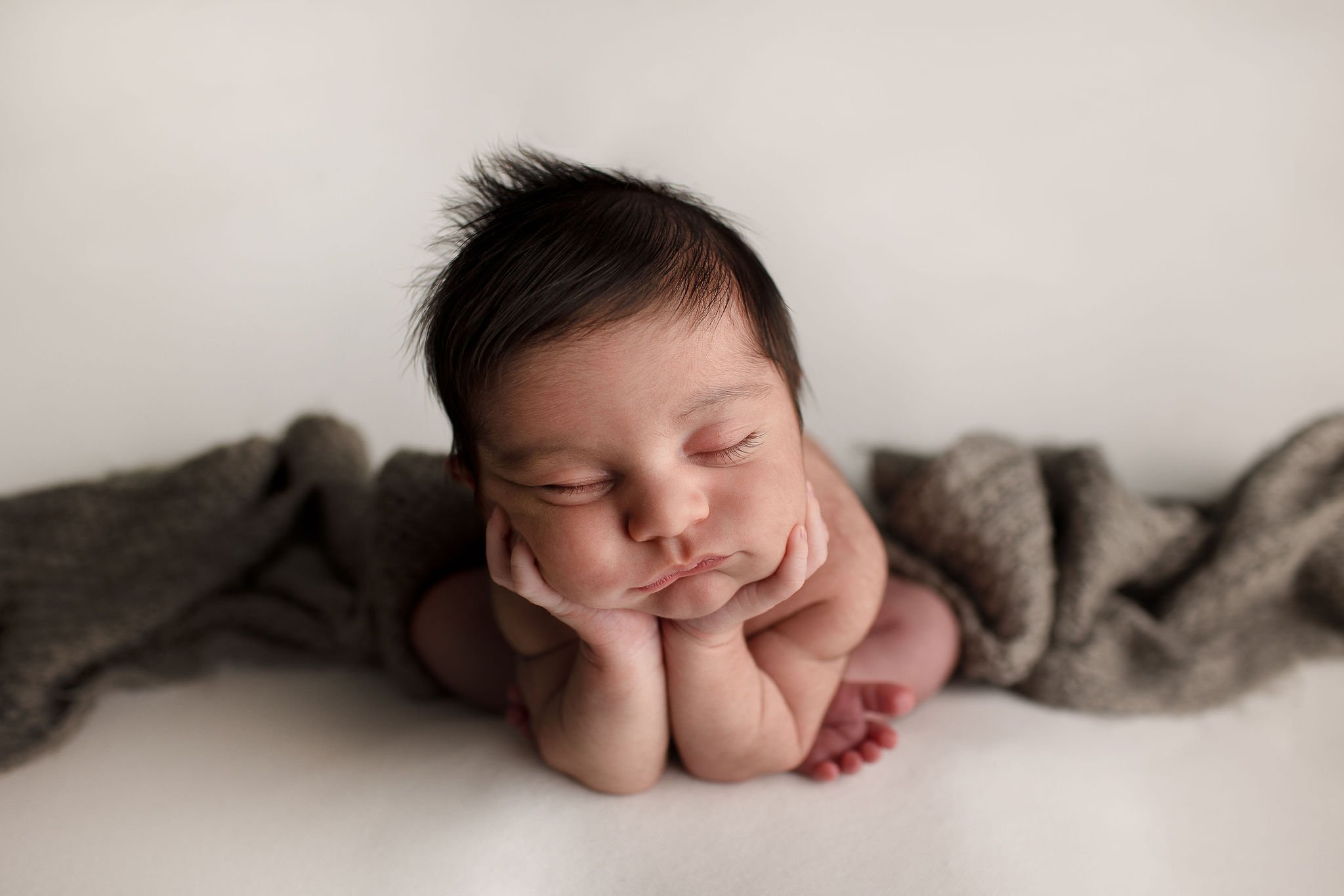  sleeping newborn baby propping his head upon his hands and elbows 