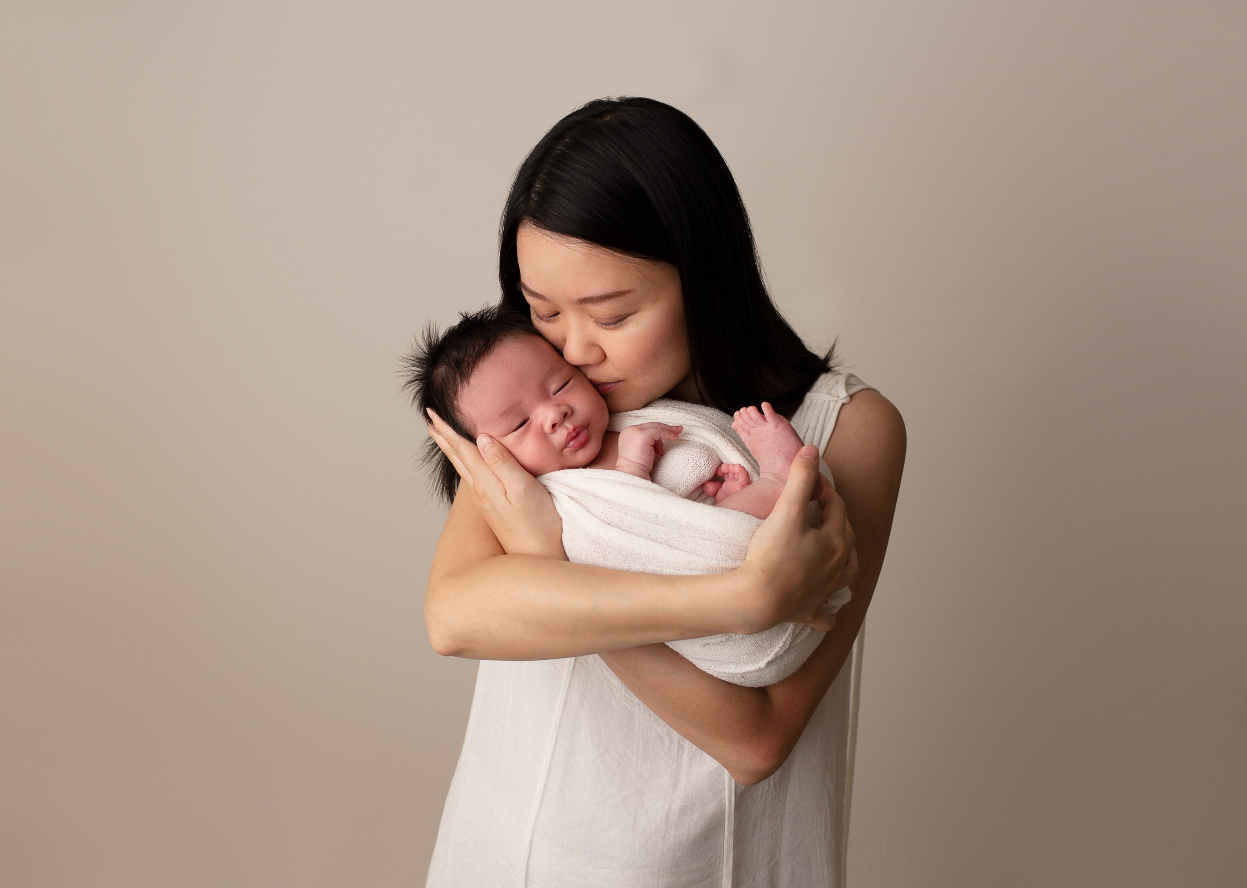  mother holding her newborn baby wrapped in a white blanet 