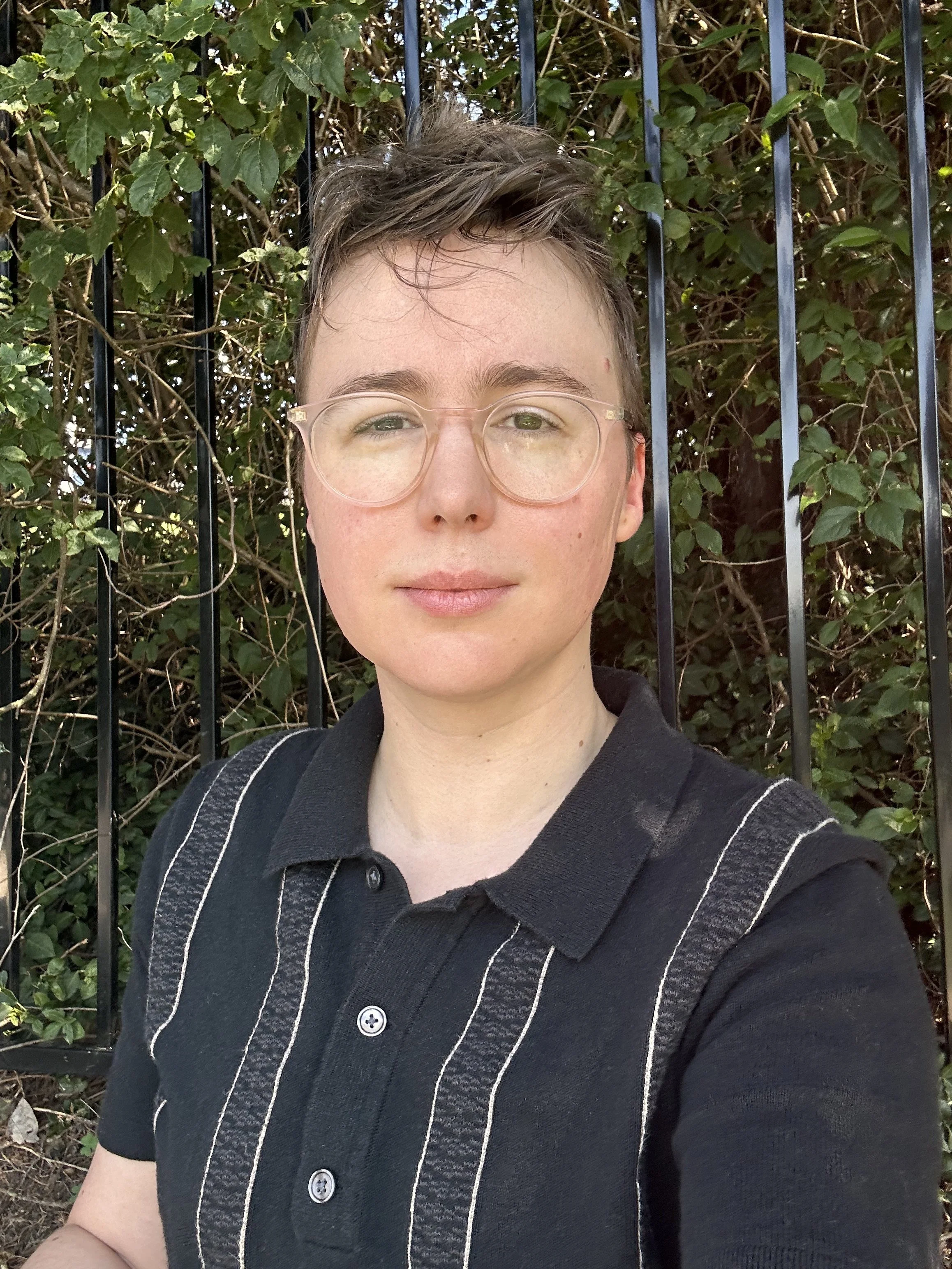 This is a photo of artist Theo Hall. They are wearing glasses and a dark polo shirt.