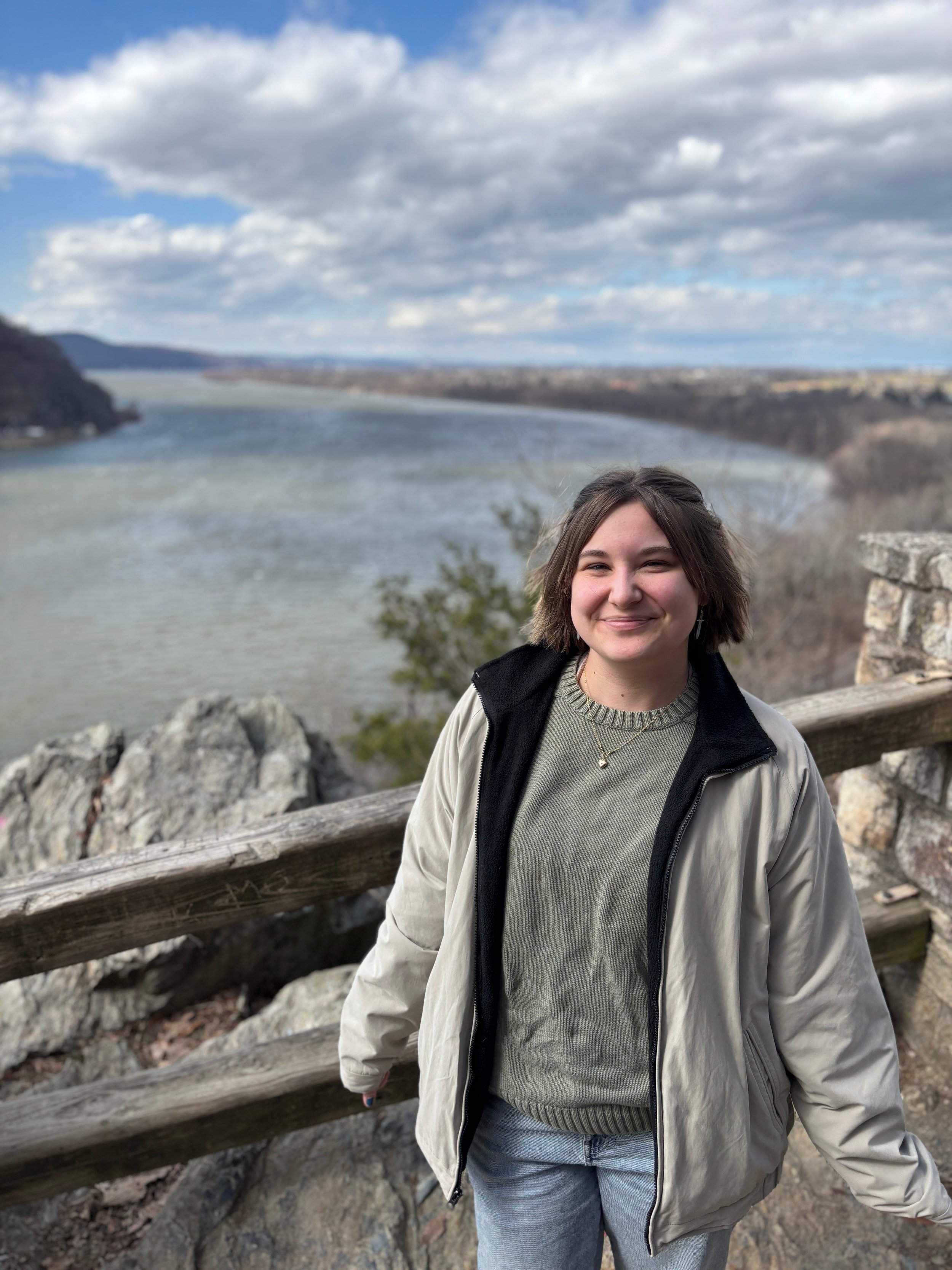 A photo of Cayla, a light-skinned person with a brown bob, standing in front of a body of water.