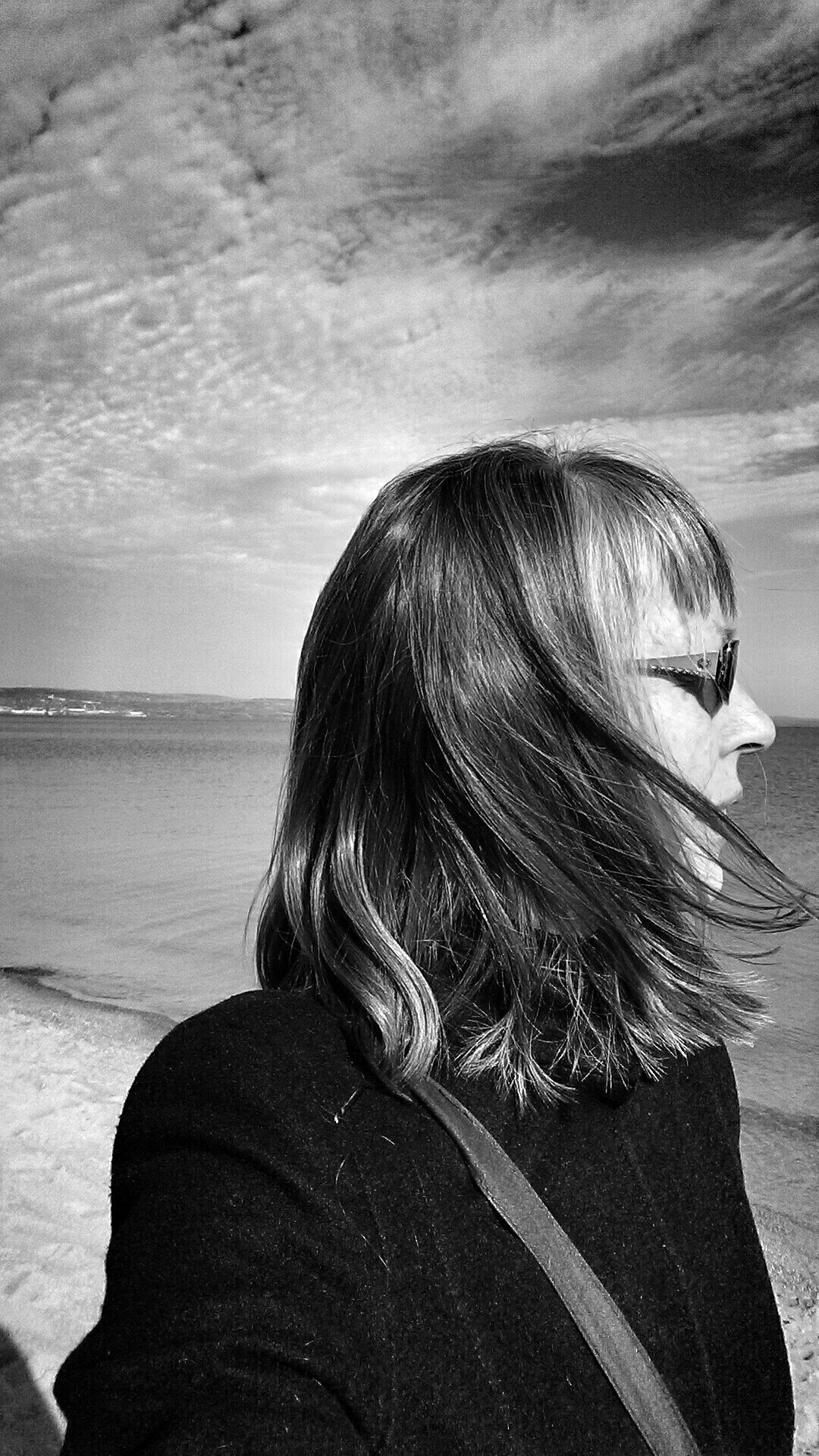 A black and white headshot of a person seen from behind and in profile. They have long hair and bangs.