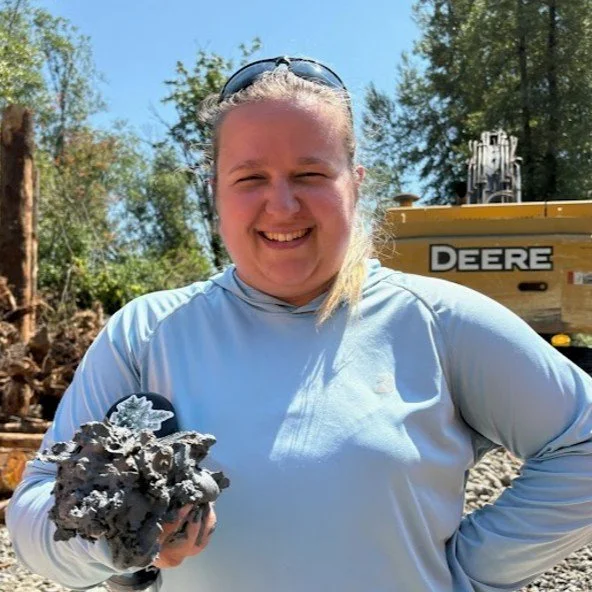 Close-up of a person with rainbow-colored hair, glasses, and a gray jacket outdoors.