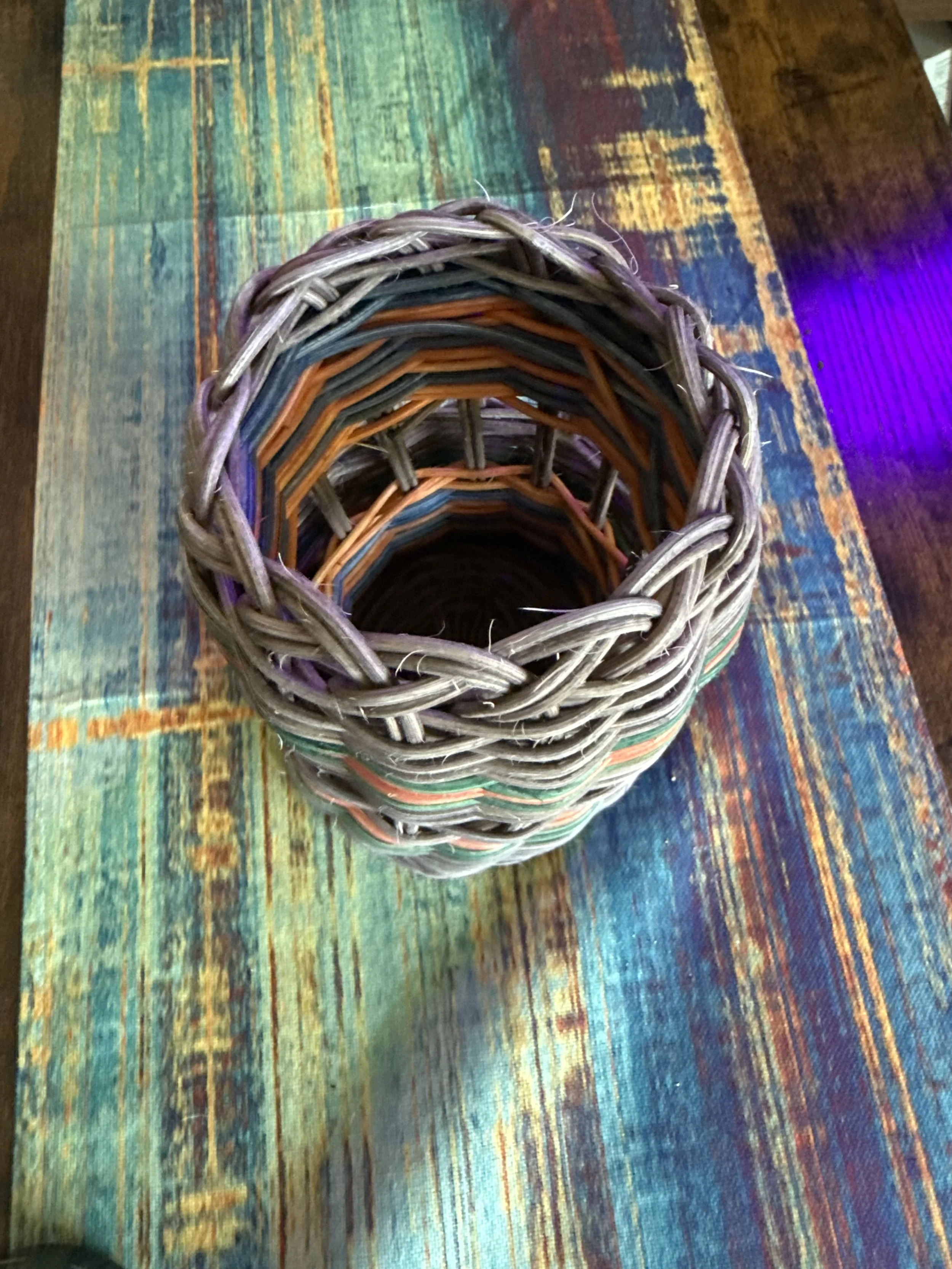 Stacked colorful woven baskets on a wooden table with a multicolored rug underneath.