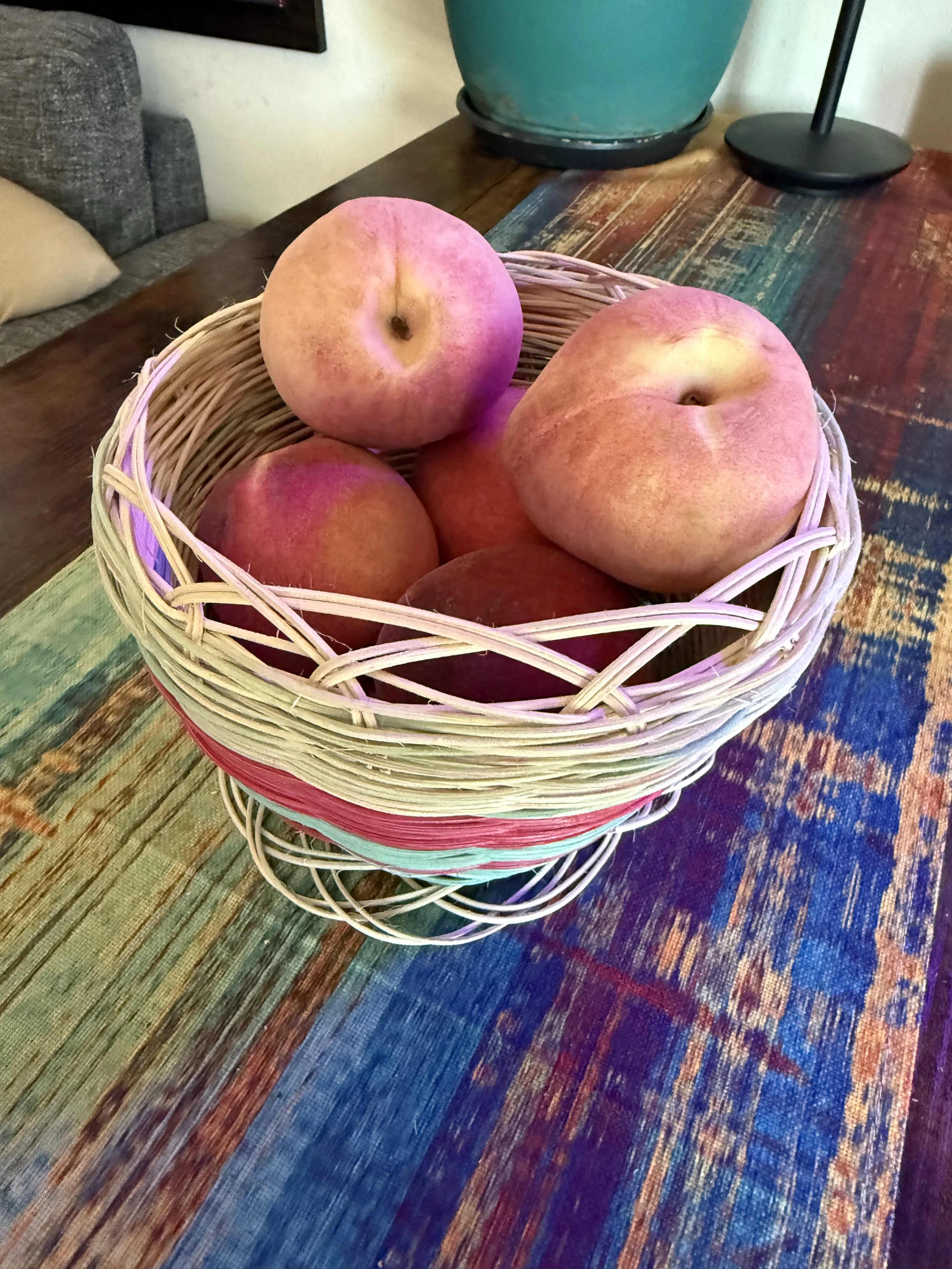 A wicker basket filled with several peaches sitting on a colorful wooden table.