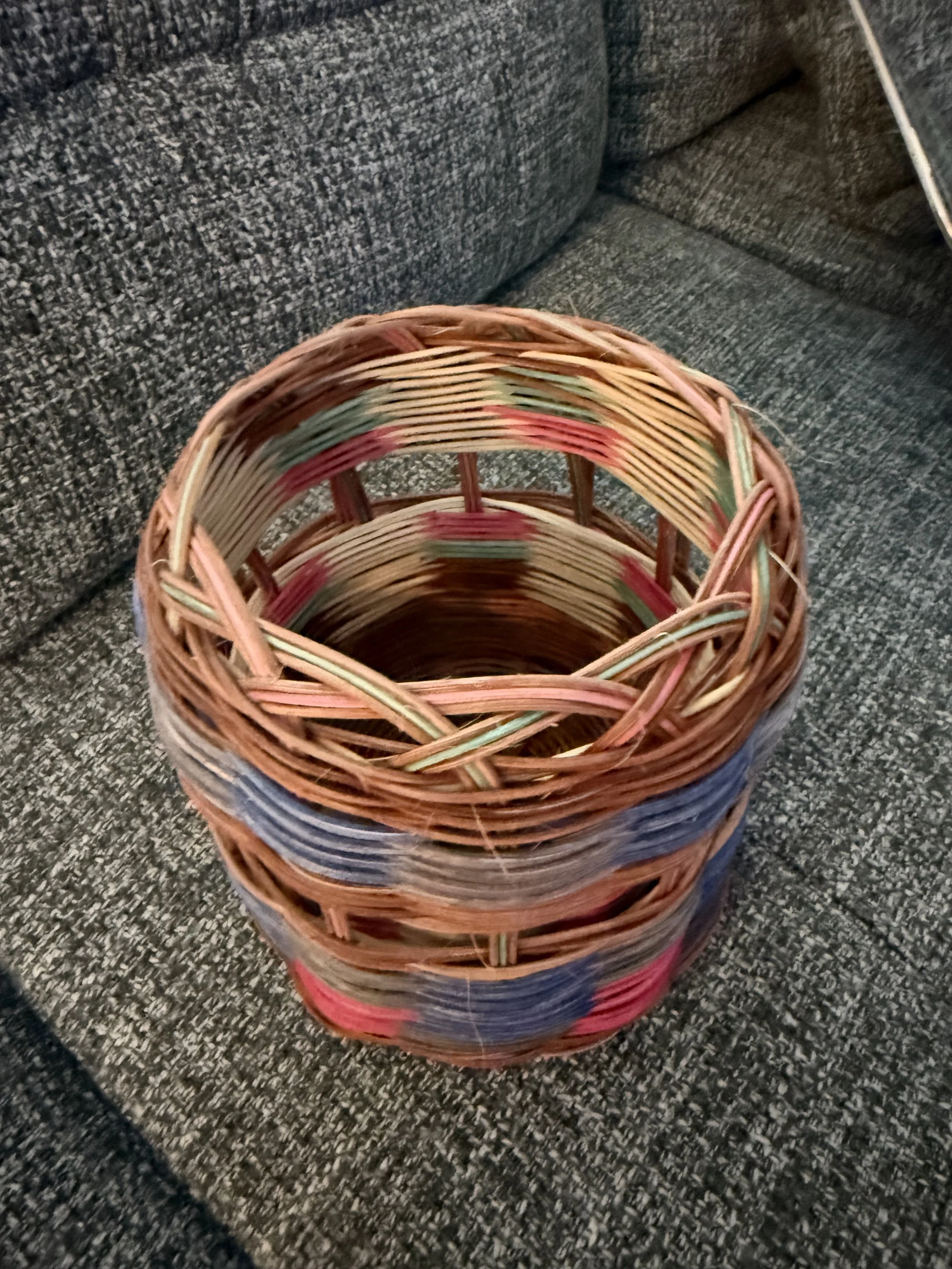 A multicolored woven basket placed on a dark gray textured carpet.