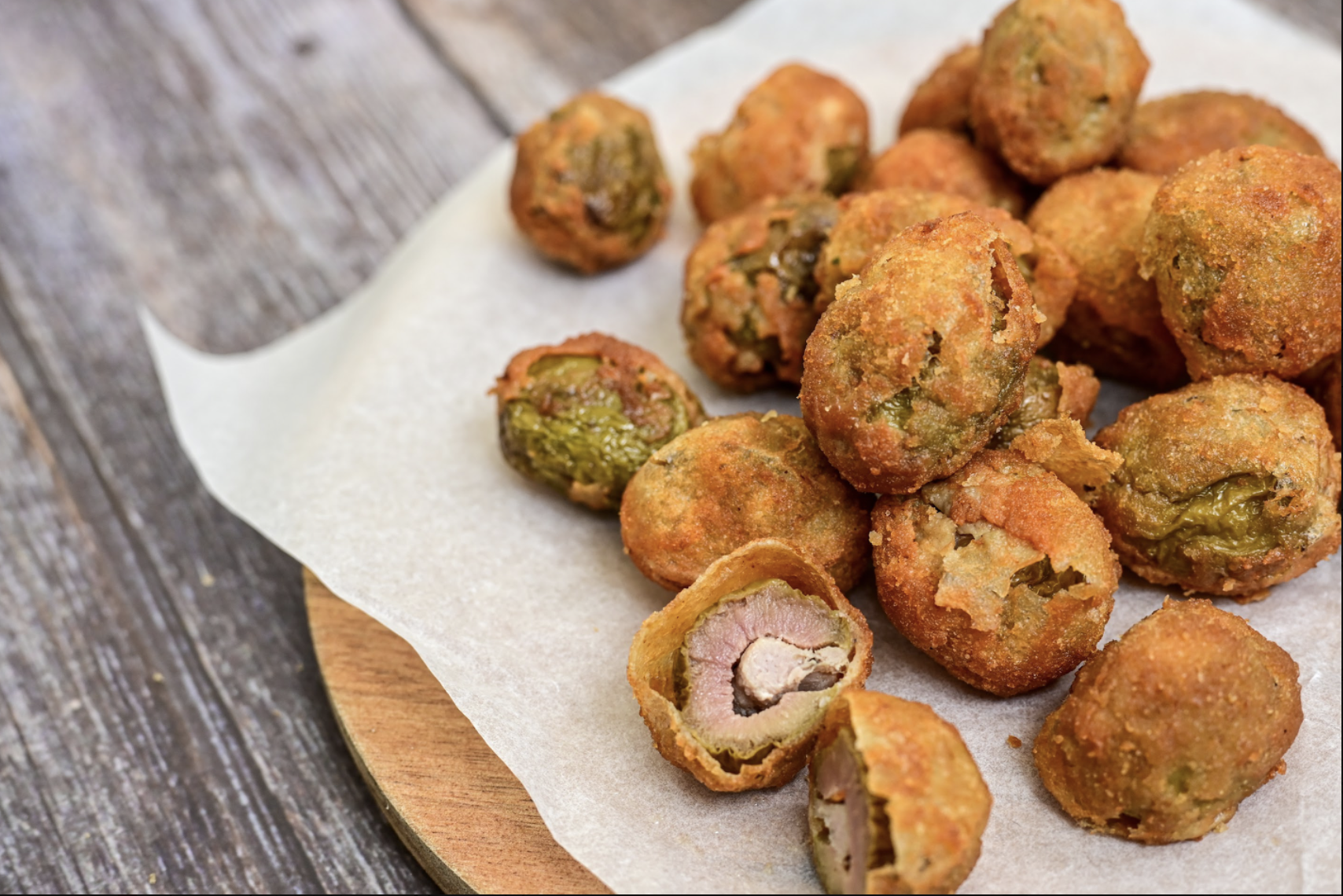 Fried appetizers filled with meats and vegetables, some cut open showing the fillings, on parchment paper on a wooden serving board.