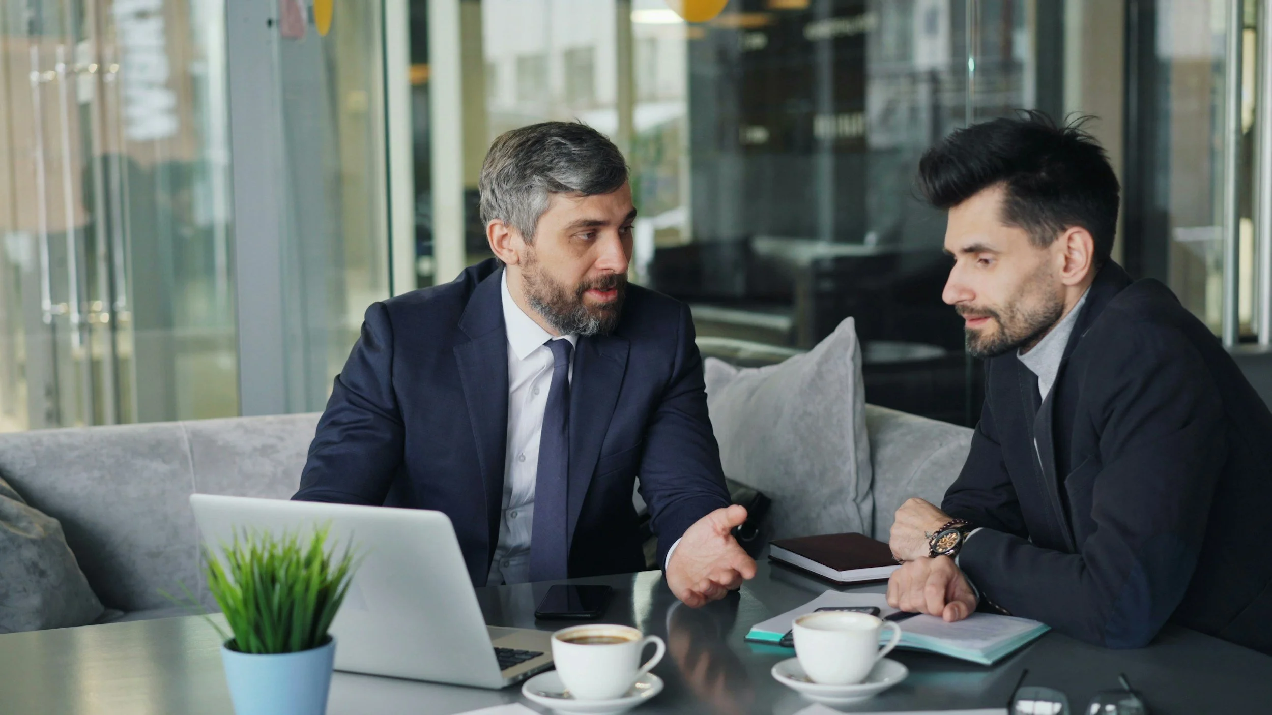 Two men in business attire engaged in a serious conversation in a modern office setting.