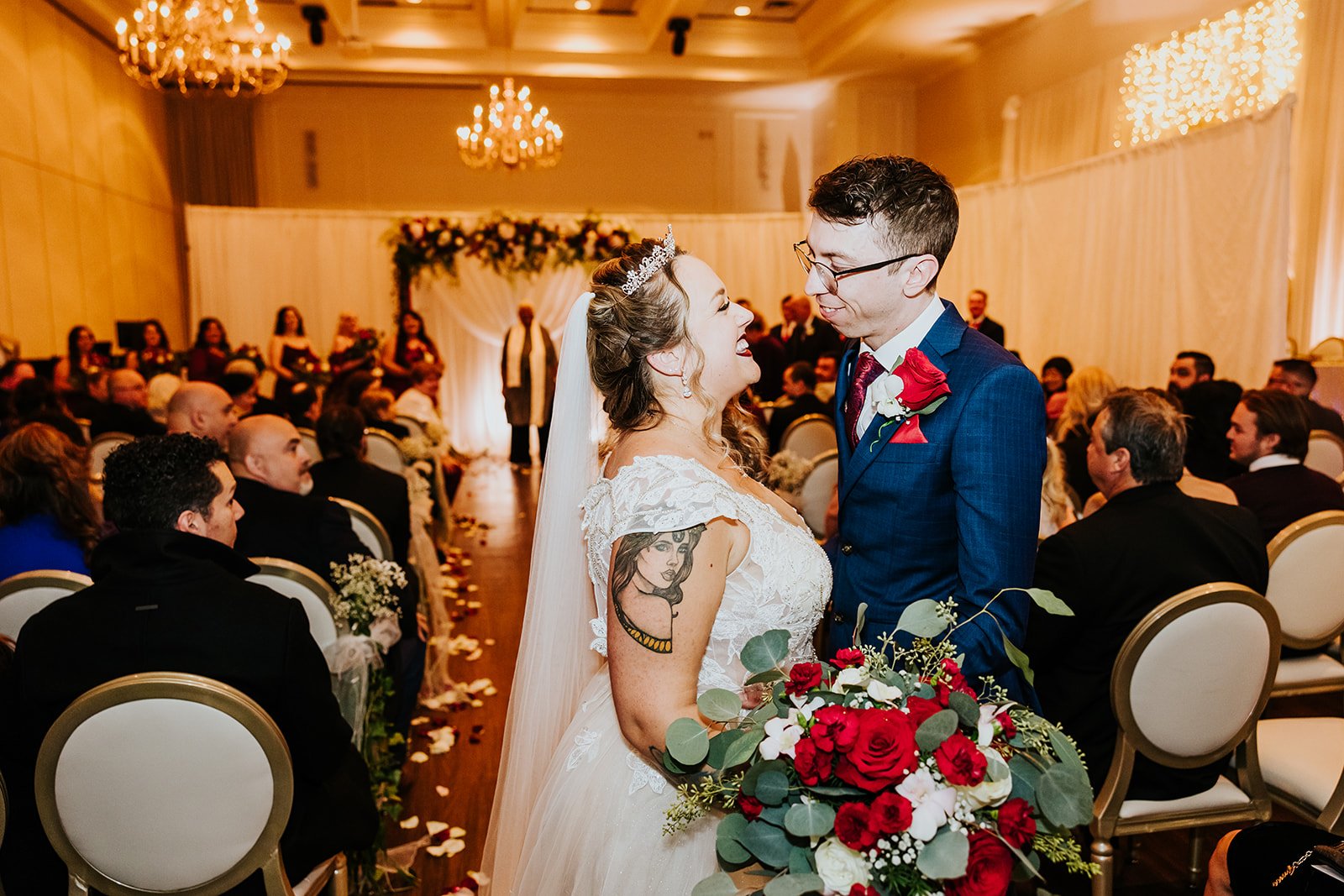 Bride and groom with red glowers kiss at the end of the isle photo by Fedora Media.jpg