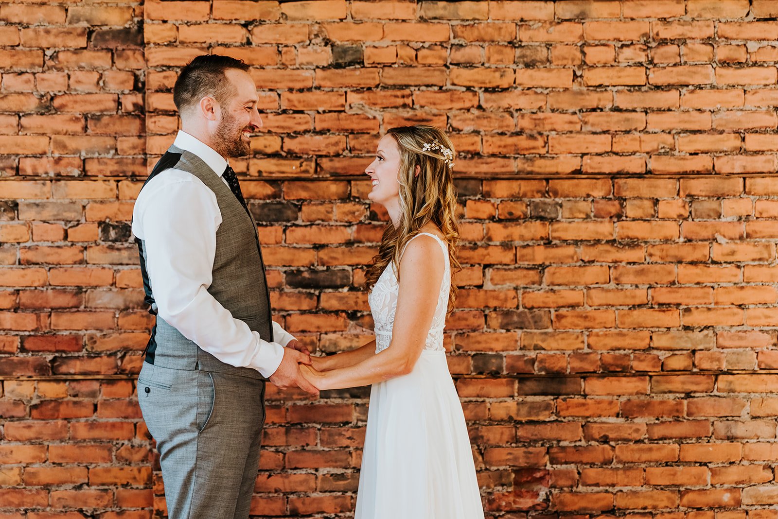 Bride and groom smile in front of a brick wall photo by Fedora media.jpg