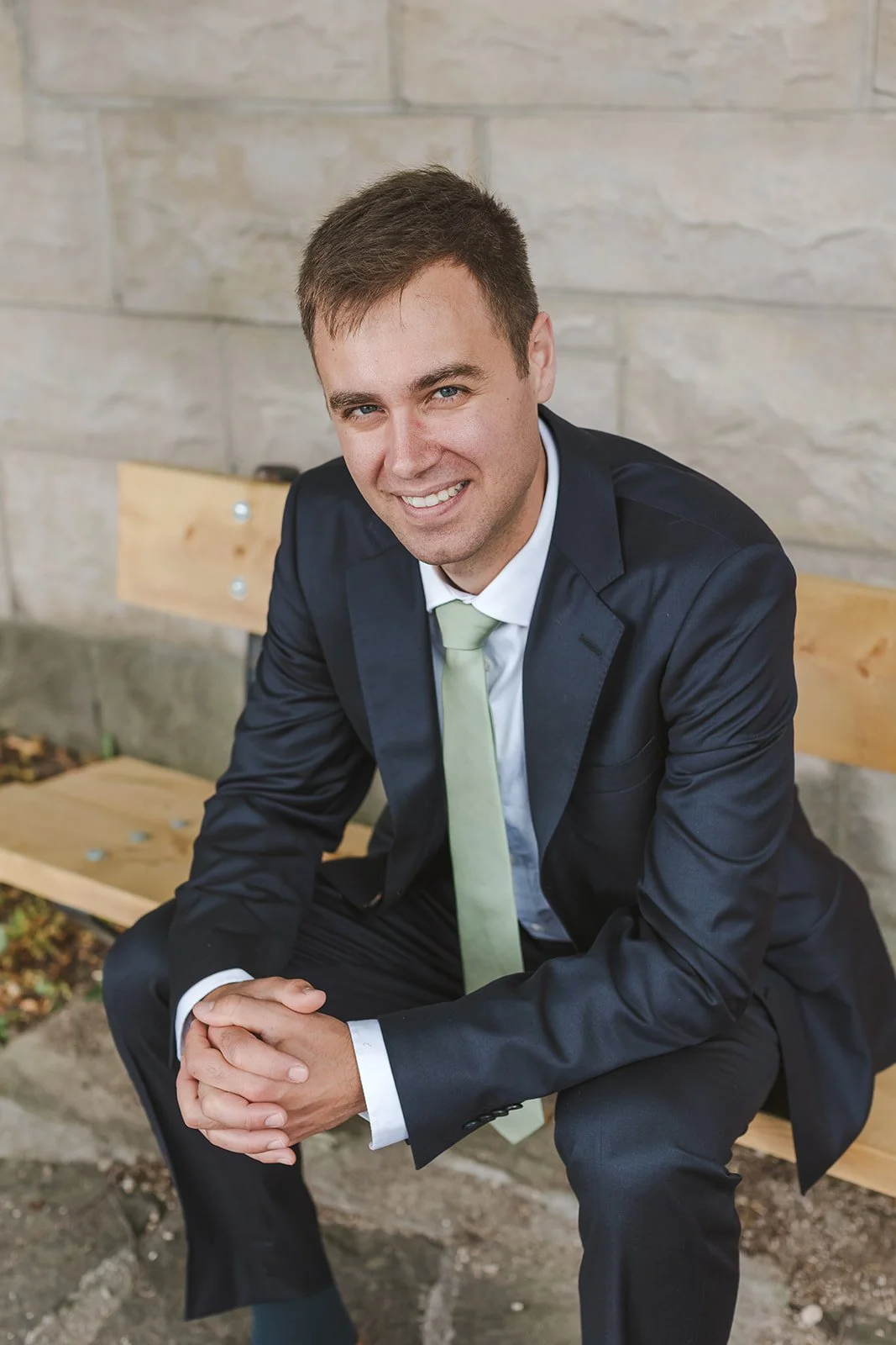 Groom Sits on Park Bench in Black Suit with Green Tie  Fedora Media  Backyard Wedding  Groom Portraits.jpg