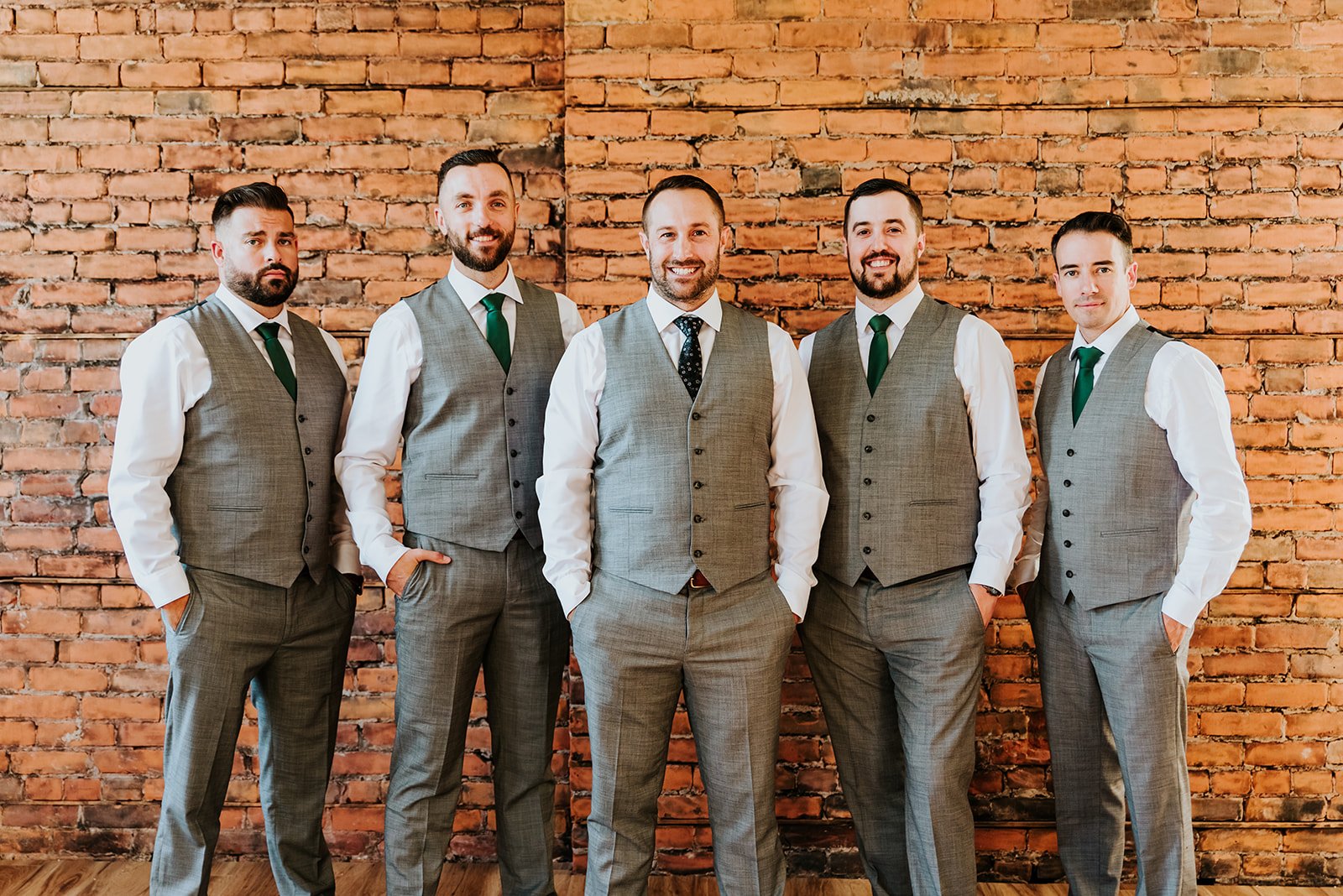 Groom poses with groomsmen in gray in front of a brick wall photo by Fedora Media.jpg