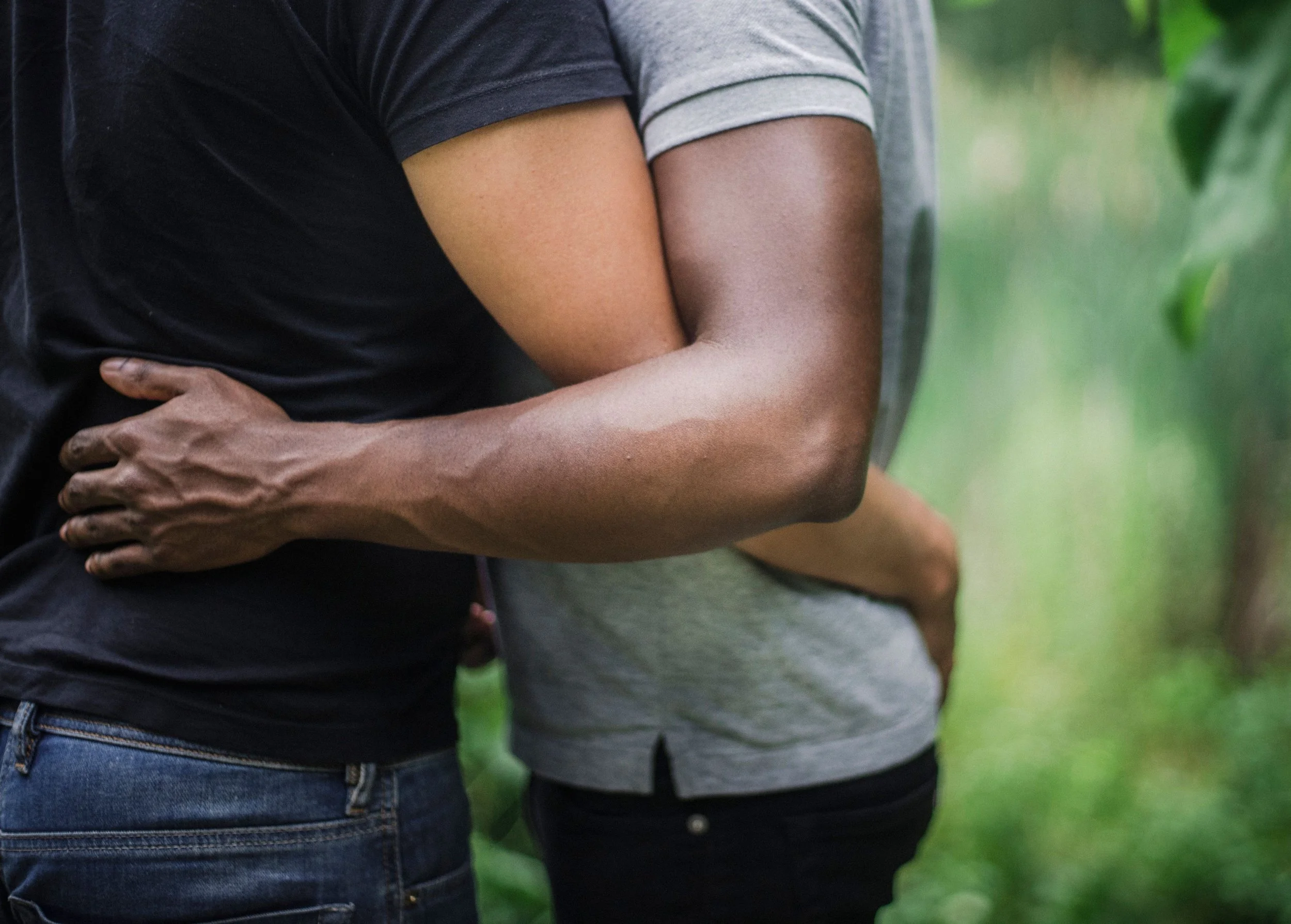 Close-up of an interracial couple embracing from behind, arms wrapped around each other