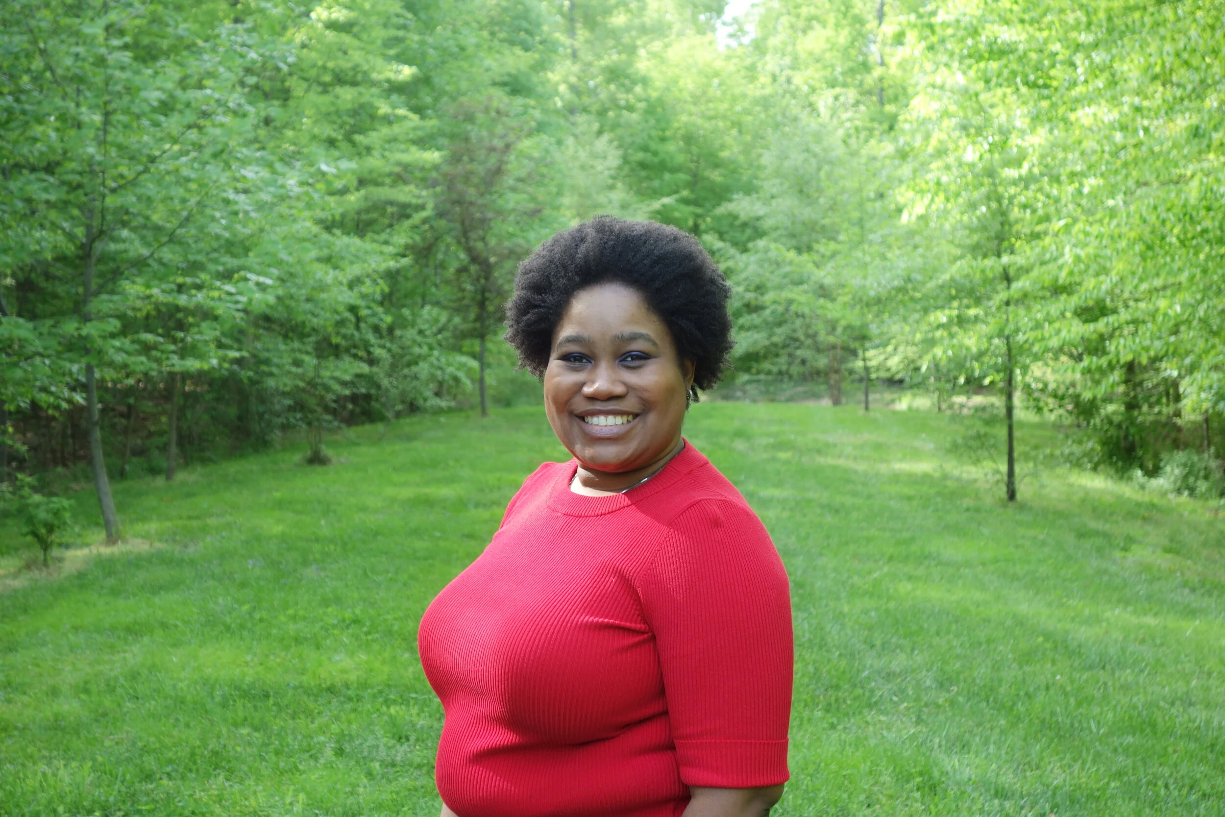 Mina Beveney, founder and trauma-informed therapist at Sunbird Counseling, smiling outdoors in front of green trees