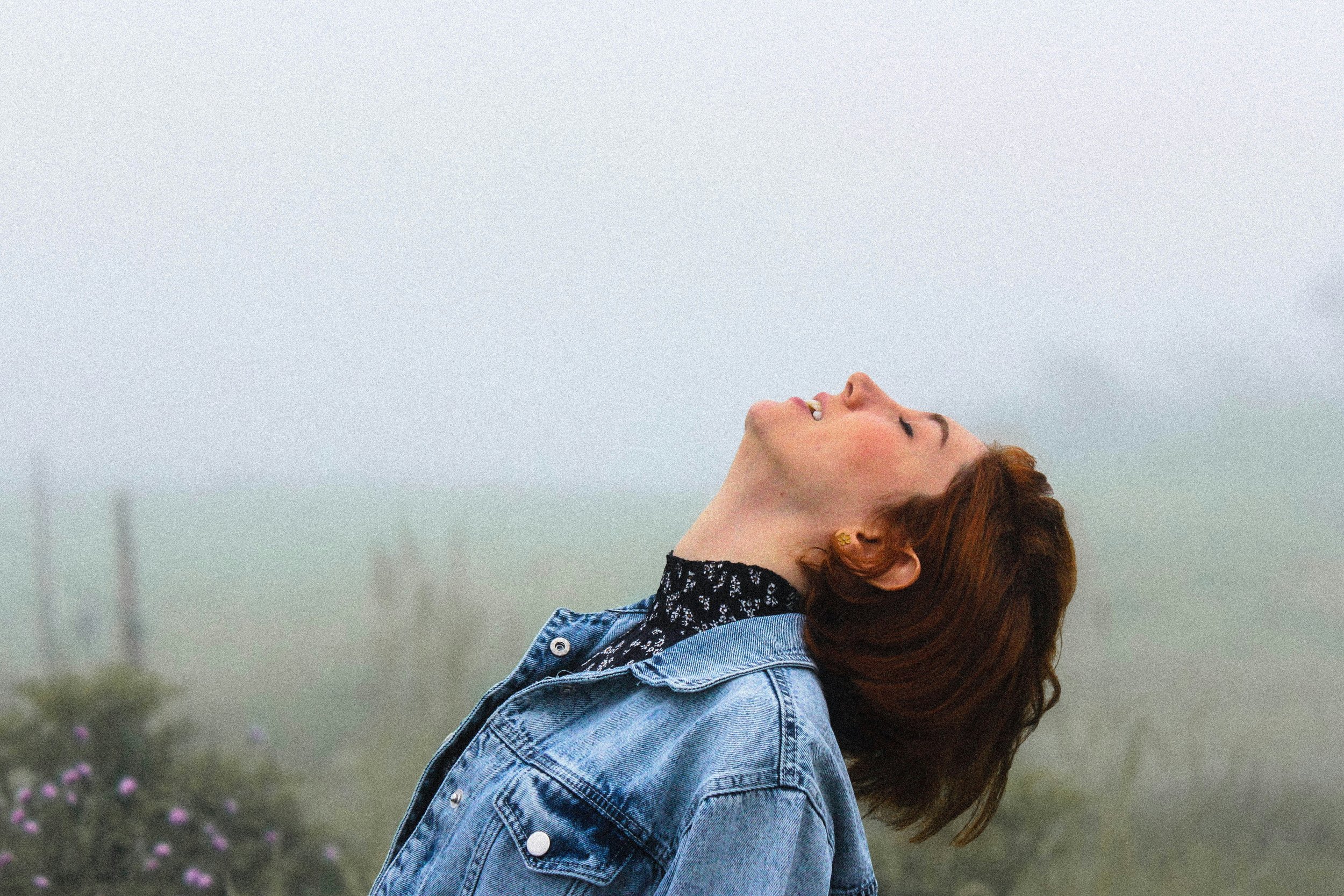Woman with her head tilted back and eyes closed in a foggy field, experiencing release