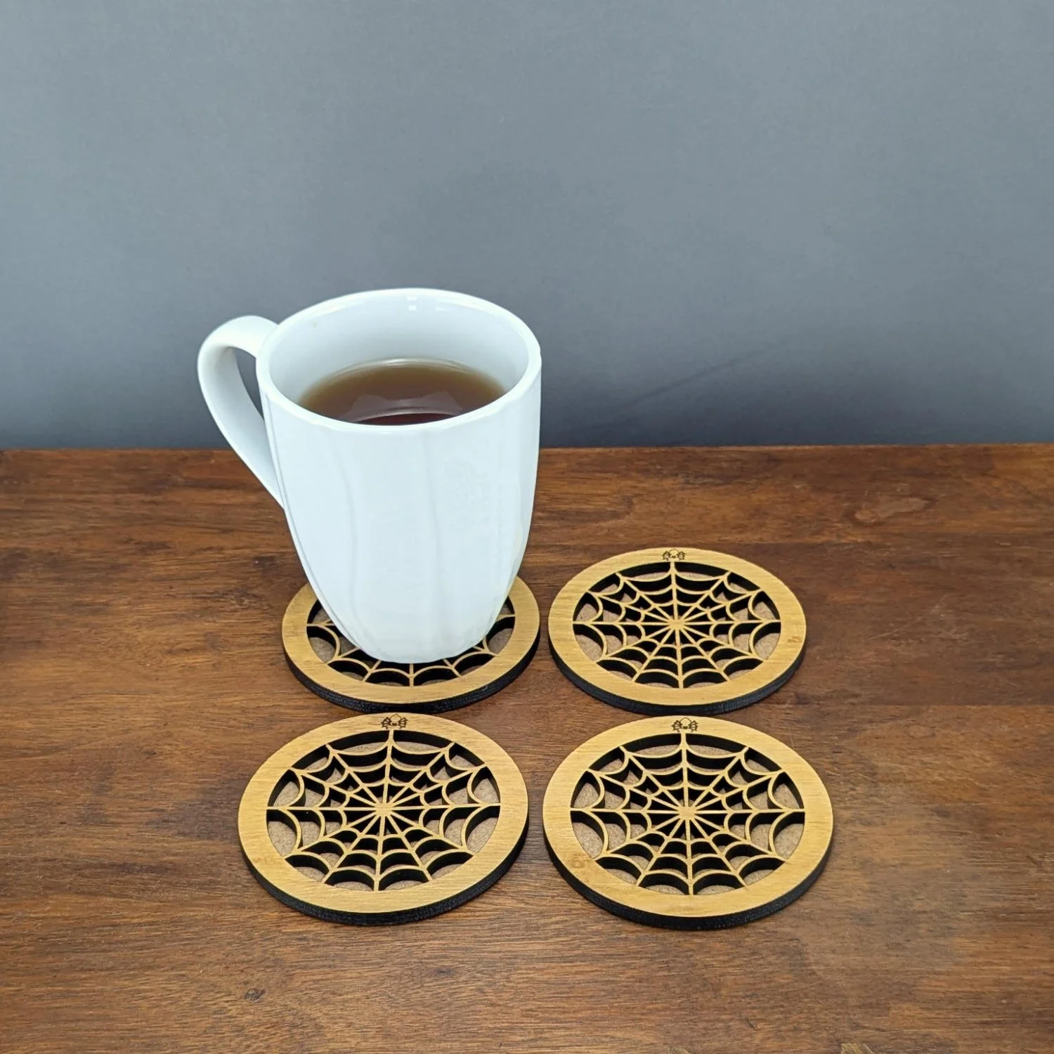 Set of four Lace Web coasters arranged on a table, one holding a white mug of tea.
