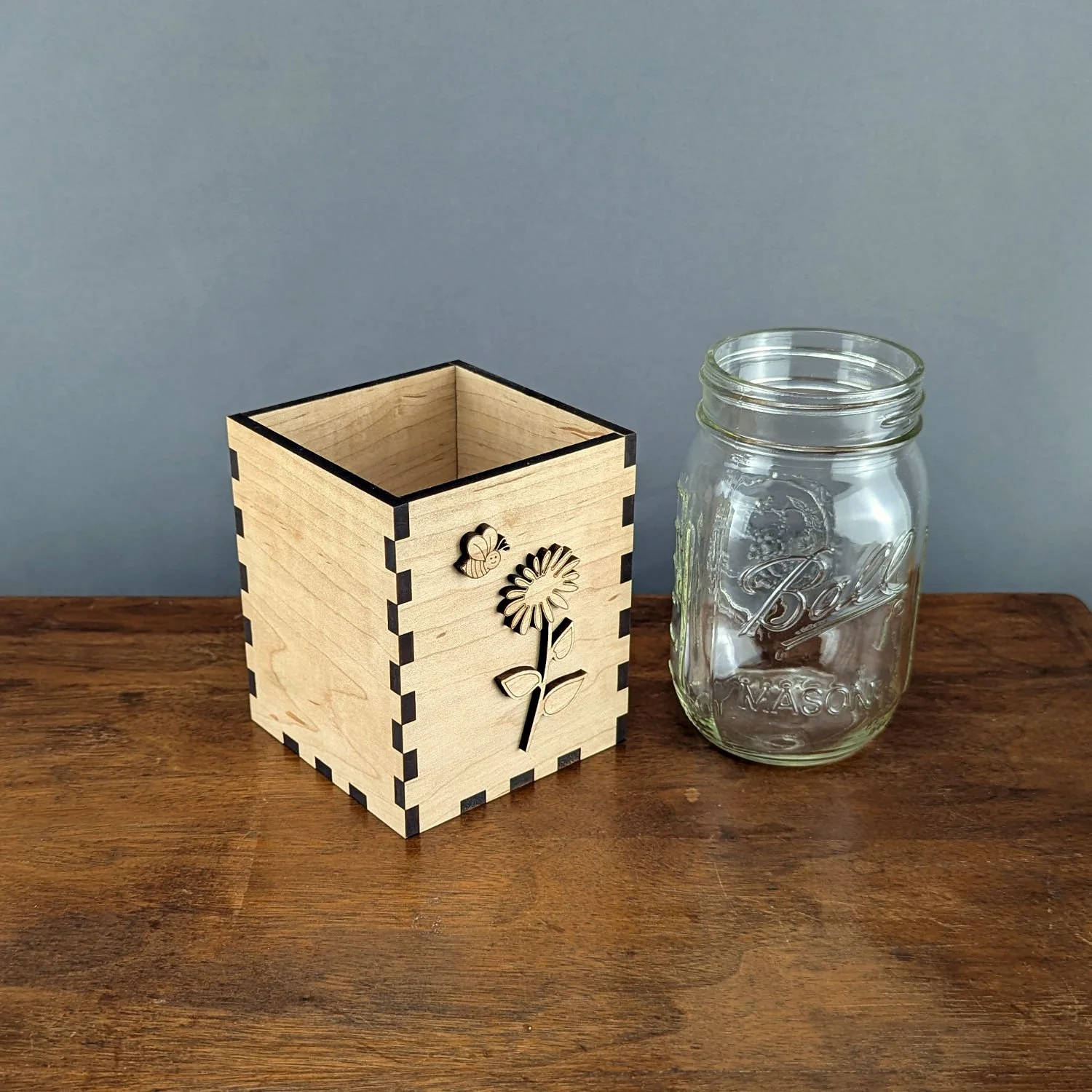 Angled front view of maple Bloom & Buzz vase box showing bee and flower laser cut design beside mason jar.
