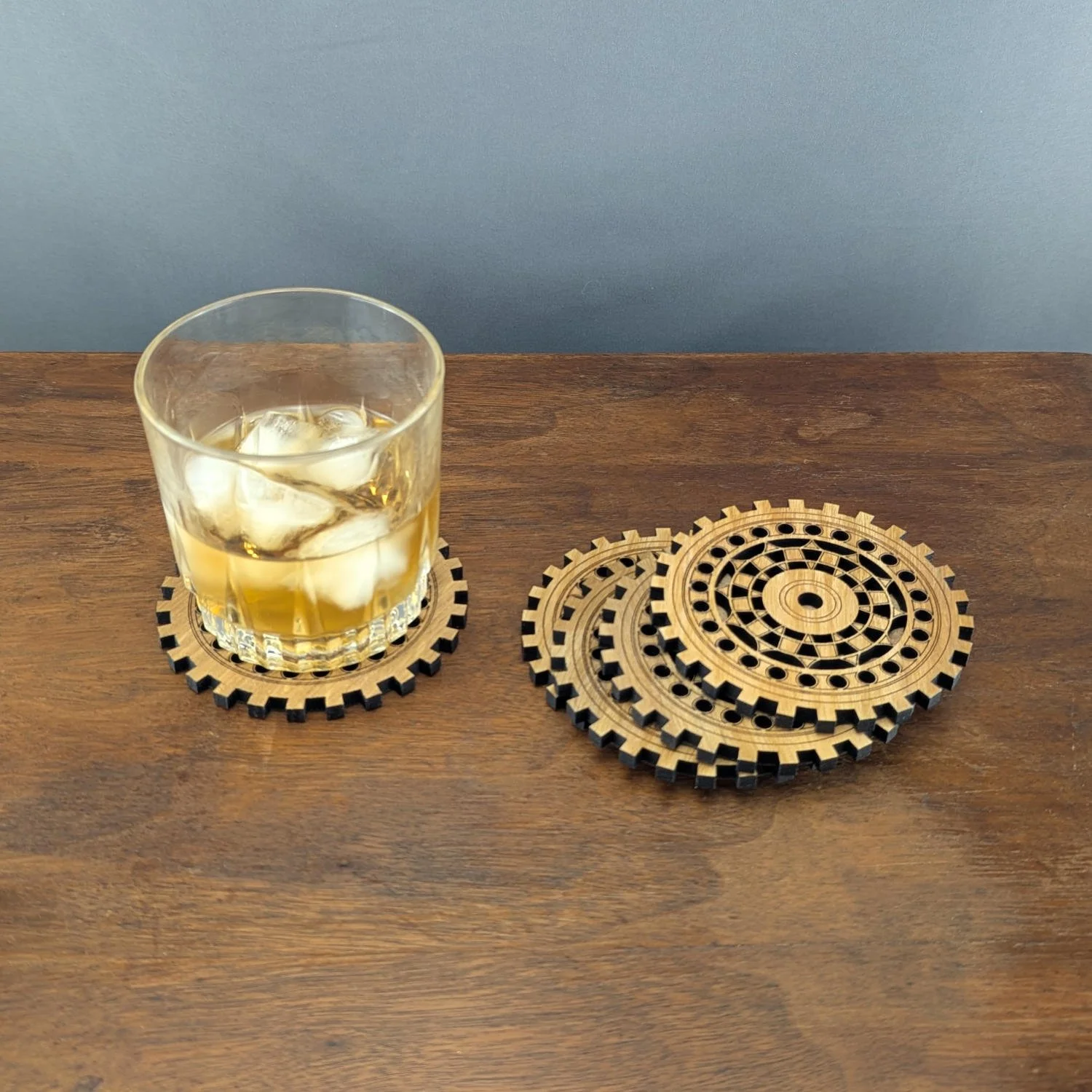 Whiskey glass on The Engineer wooden gear coaster with stack of matching coasters beside it.