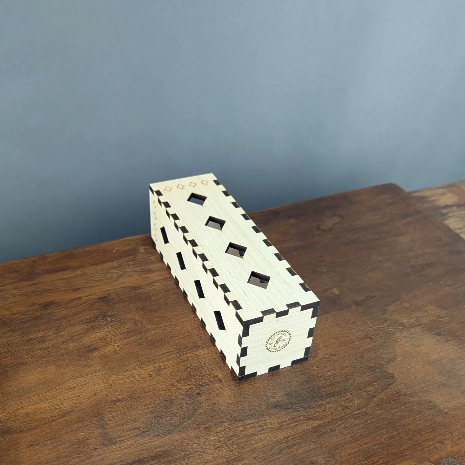 Maple vase sleeve shown laying flat on wooden table, highlighting laser-cut diamond pattern and corner joinery.