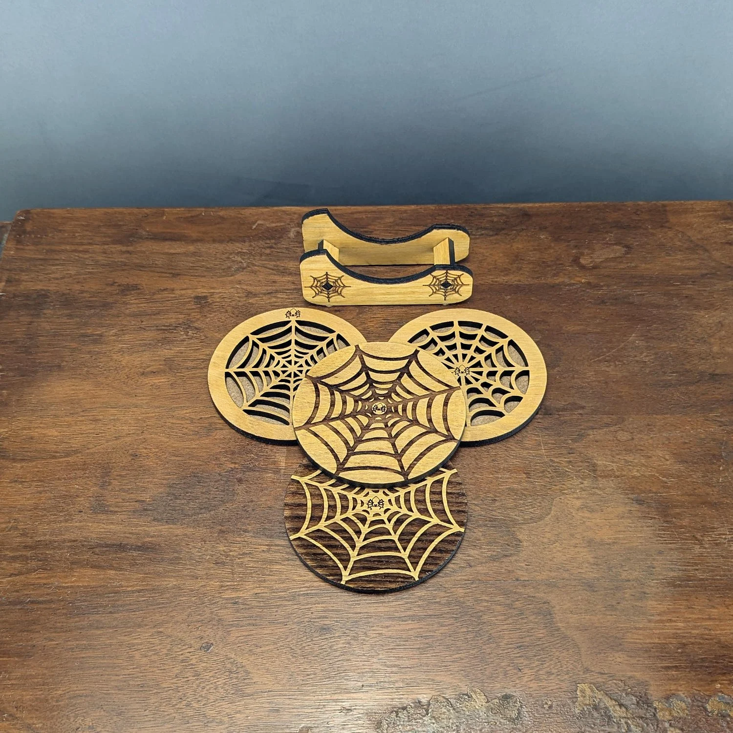 Top view of four unique spiderweb wooden coasters with engraved holder, part of the Webworks Collection Set One.