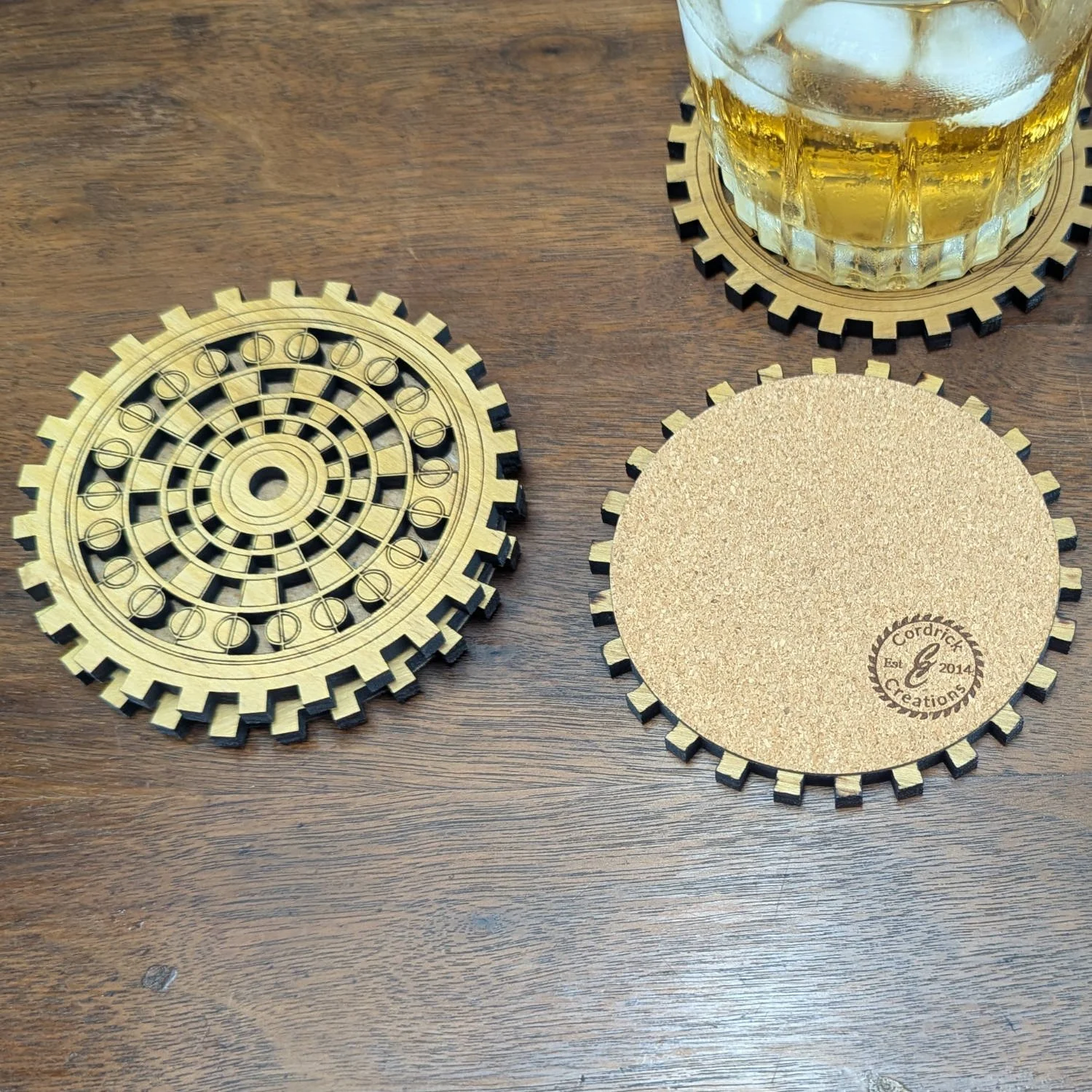 Front and back of The Operator coasters displayed, one showing cork backing with logo, the other showing engraved gear pattern.
