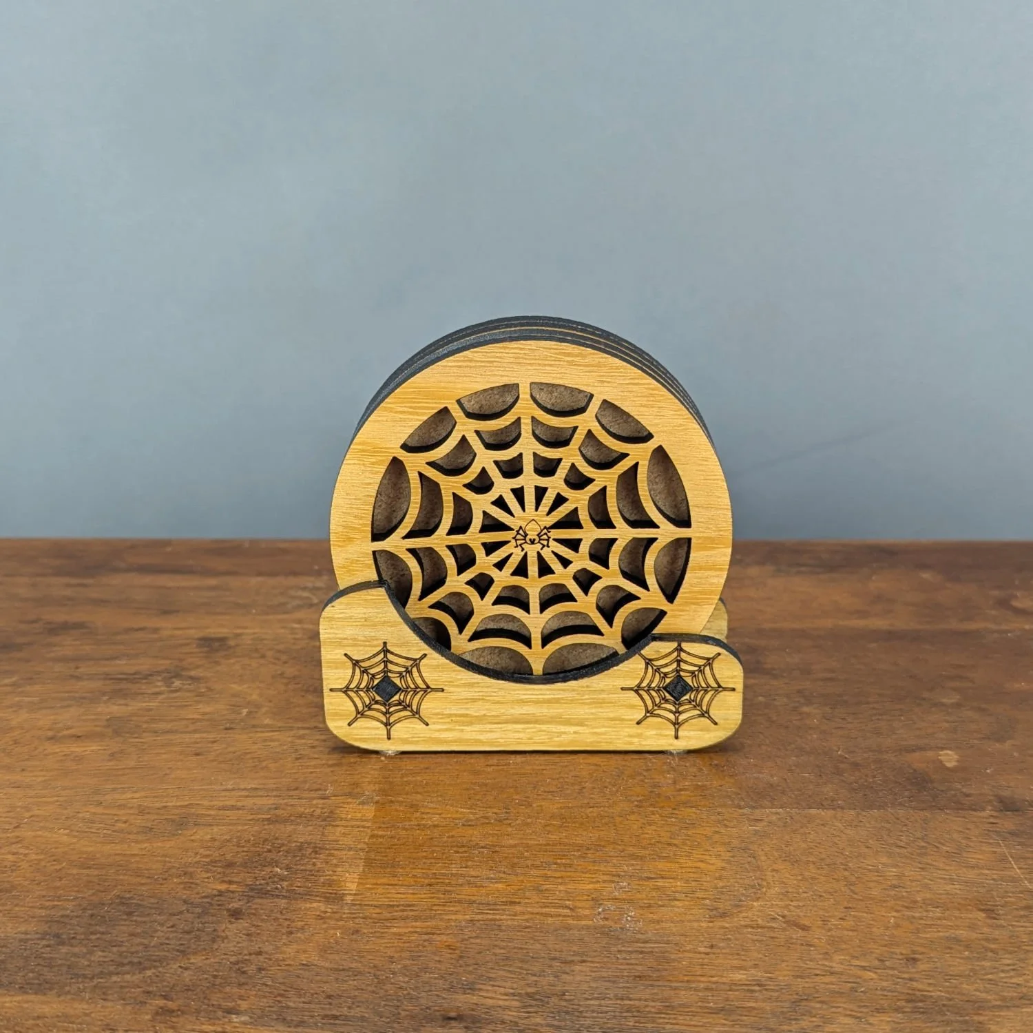 Laser-cut Iron Web wooden drink coaster set displayed in engraved spiderweb holder