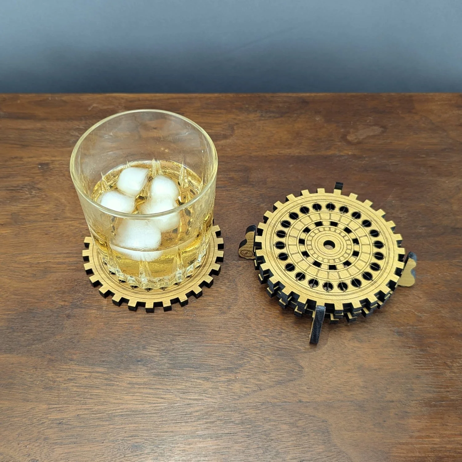 A whiskey glass on one coaster next to a stack of additional coasters neatly placed in a matching wooden holder.