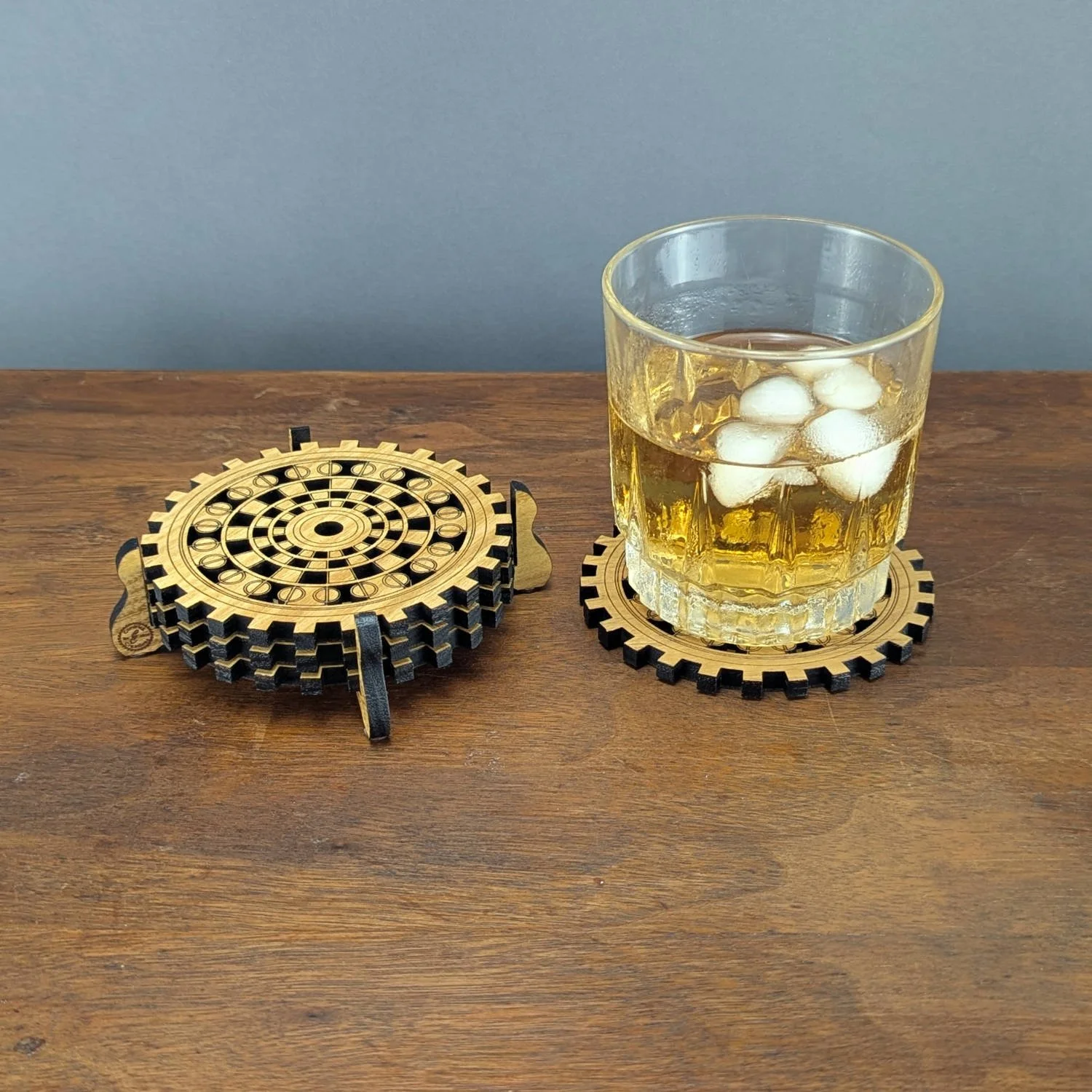 Stack of The Operator wooden gear coasters in stand next to a glass of whiskey resting on another coaster.