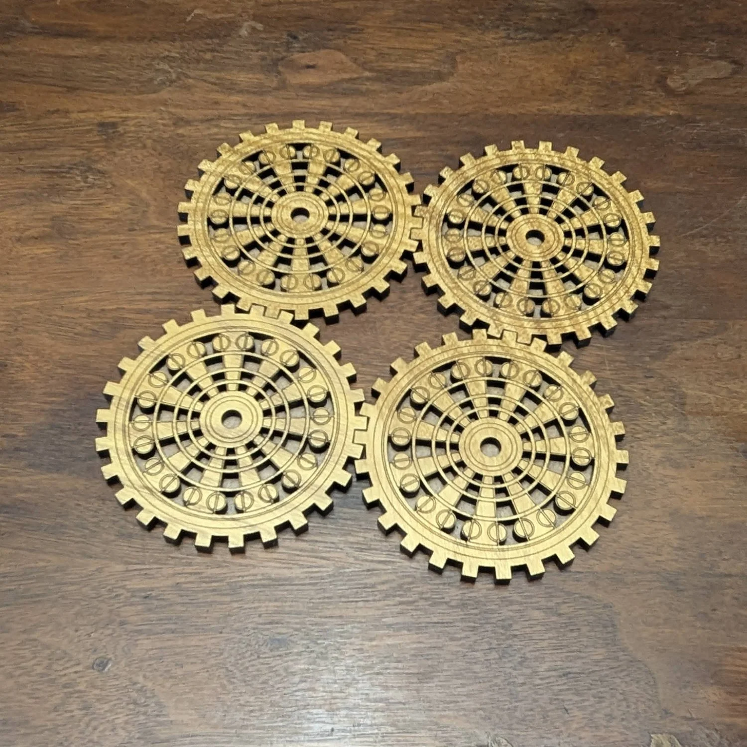 Set of four wooden gearwork coasters arranged on a wooden surface, showing detailed engraved screw and gear design.